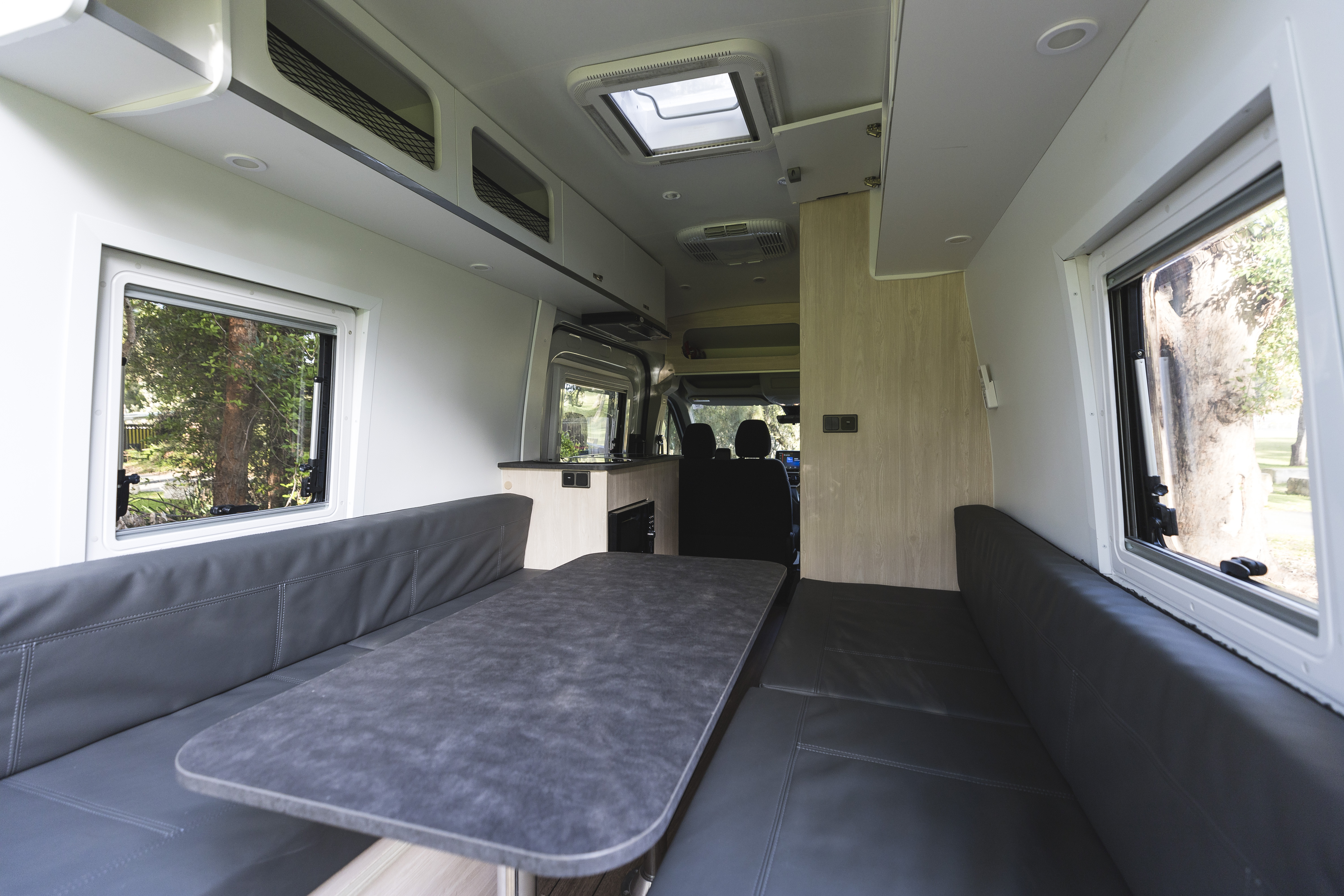 Interior of a campervan with a dining table, cushioned benches, and large windows on both sides.