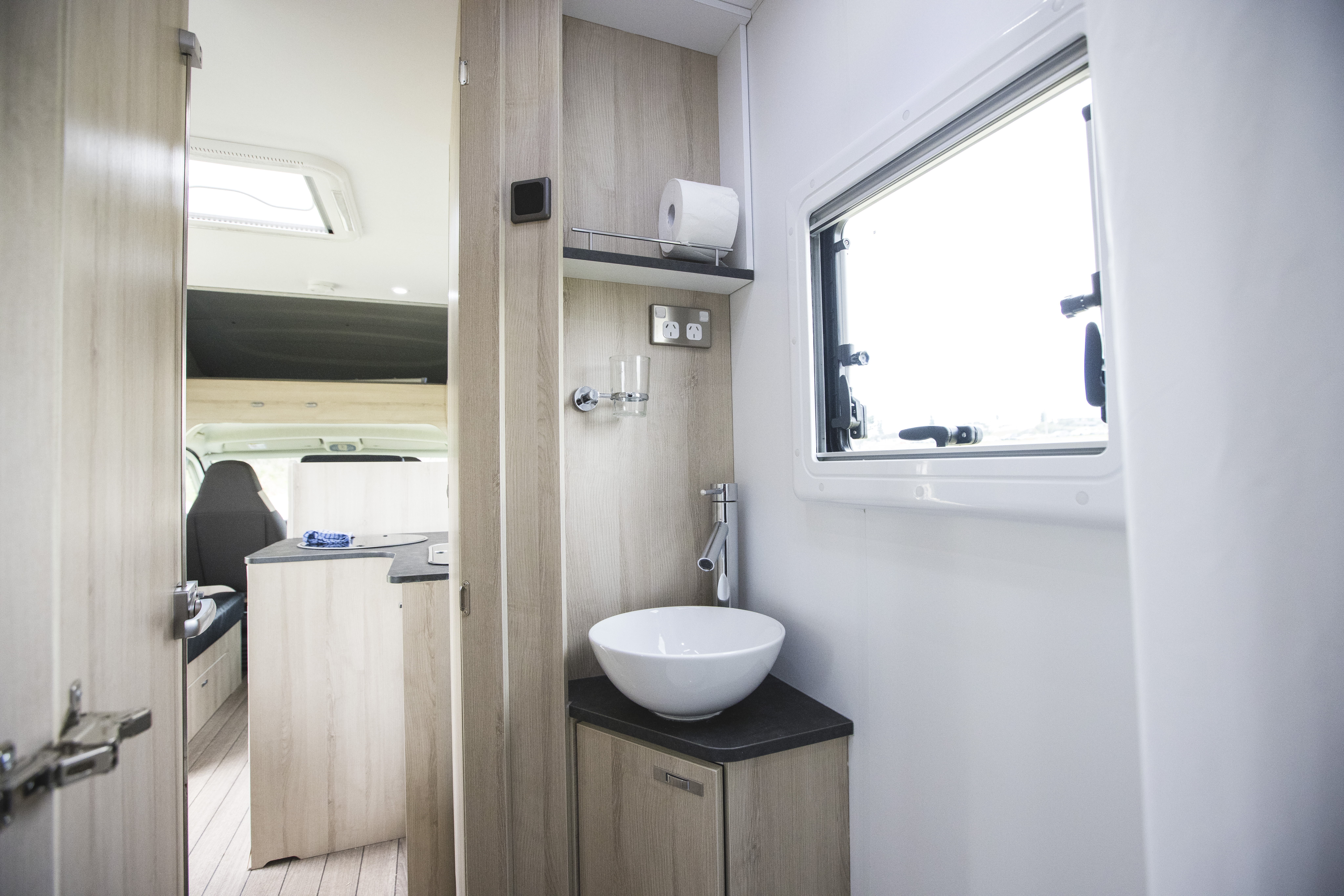 Modern campervan interior with compact sink, countertop, storage cabinets, and a window, showcasing bright, clean design.