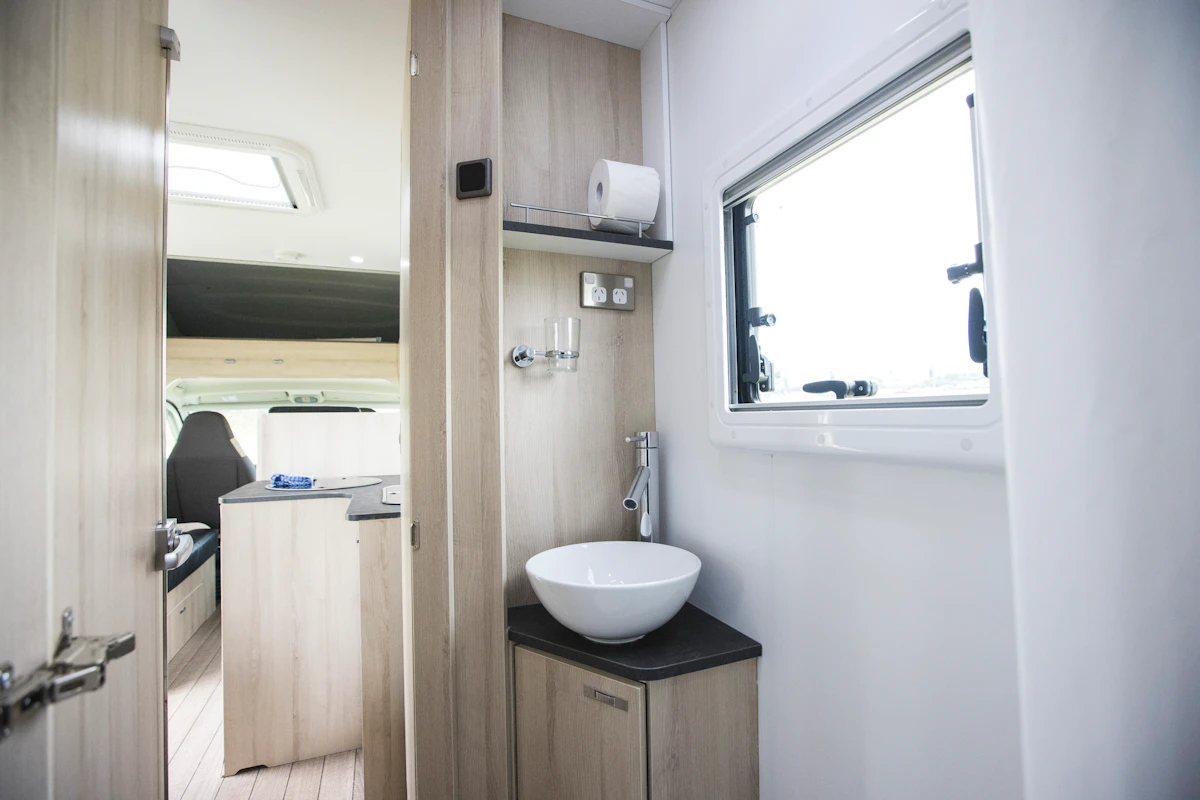 Modern campervan interior with compact sink, countertop, storage cabinets, and a window, showcasing bright, clean design.