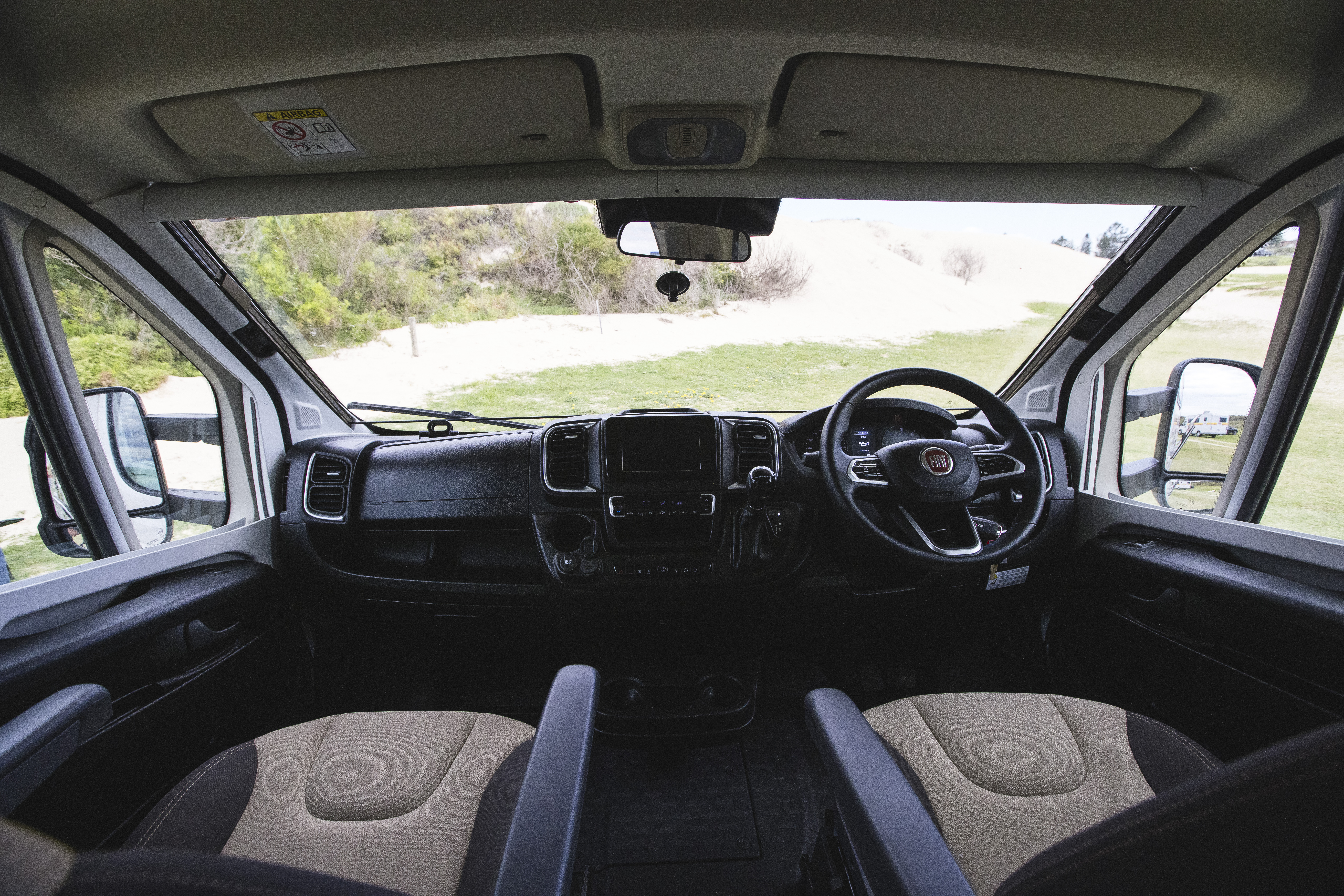 Spacious campervan interior with two front seats, modern dashboard, and a scenic outdoor view through the windshield.