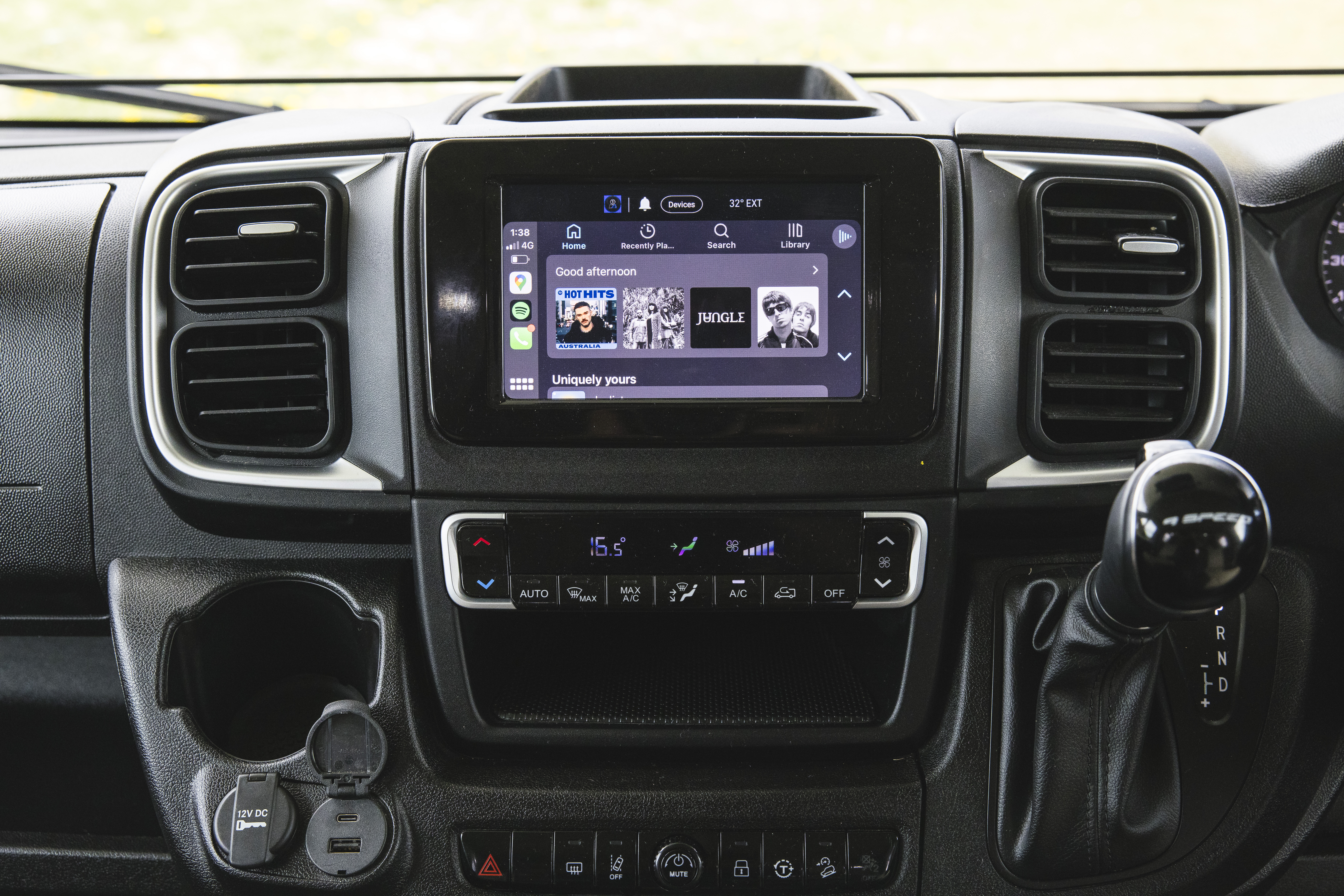 Interior view of campervan dashboard featuring touchscreen display, climate controls, gear shift, and cup holder.
