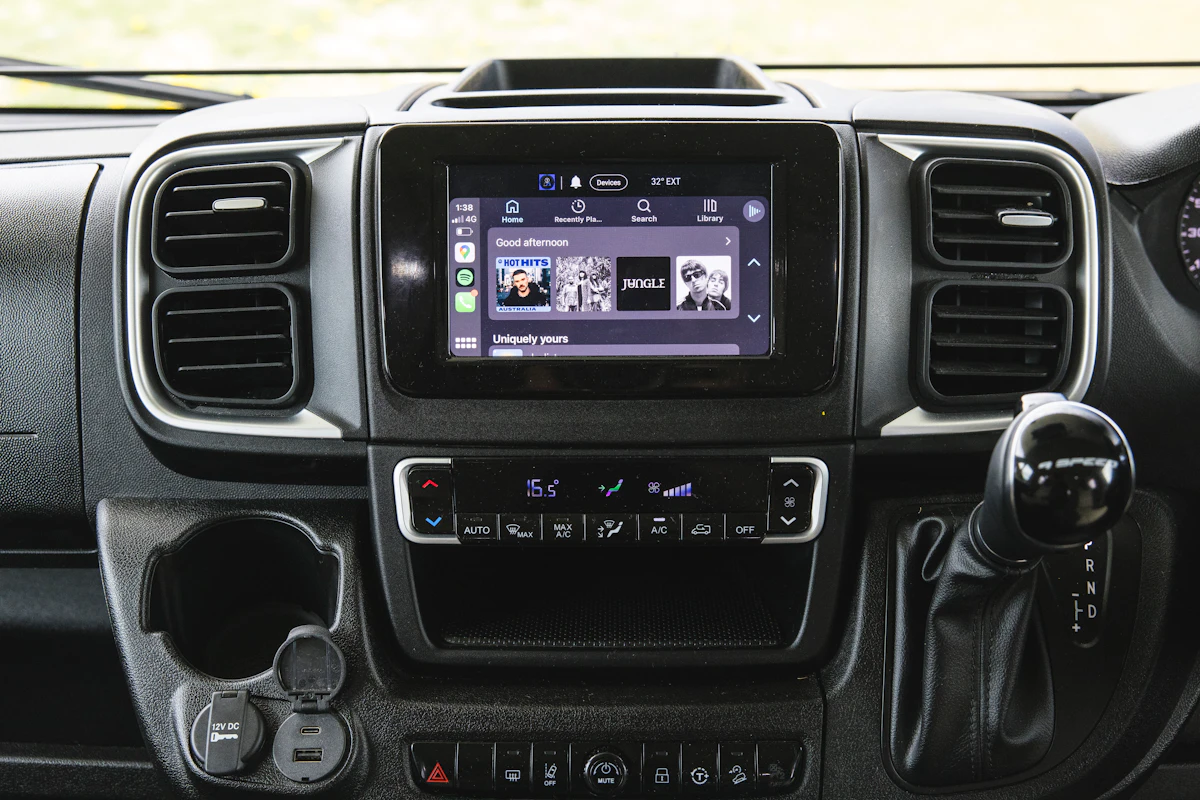 Interior view of campervan dashboard featuring touchscreen display, climate controls, gear shift, and cup holder.