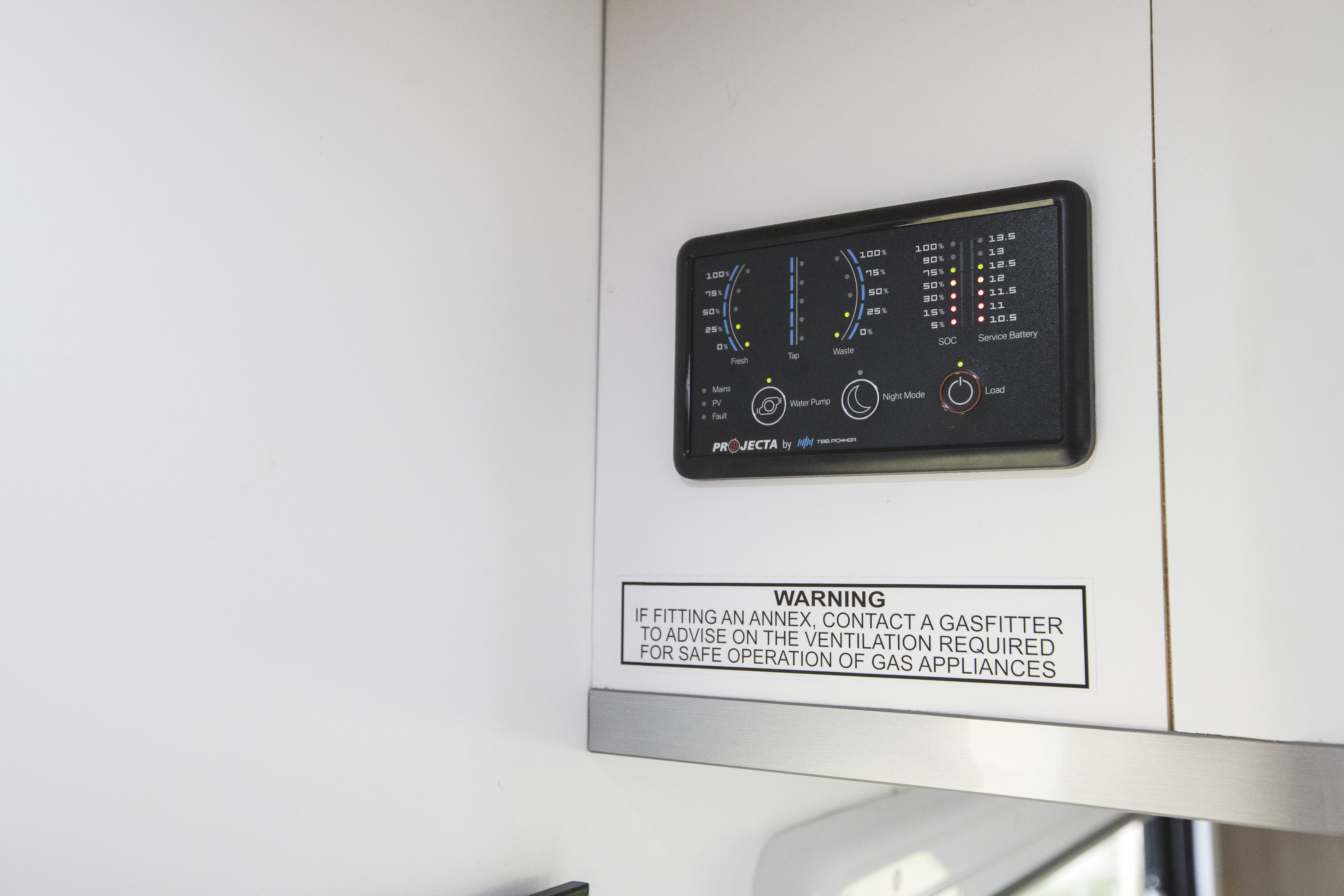 Close-up of a campervan control panel with warning label for safe operation of gas appliances below it.