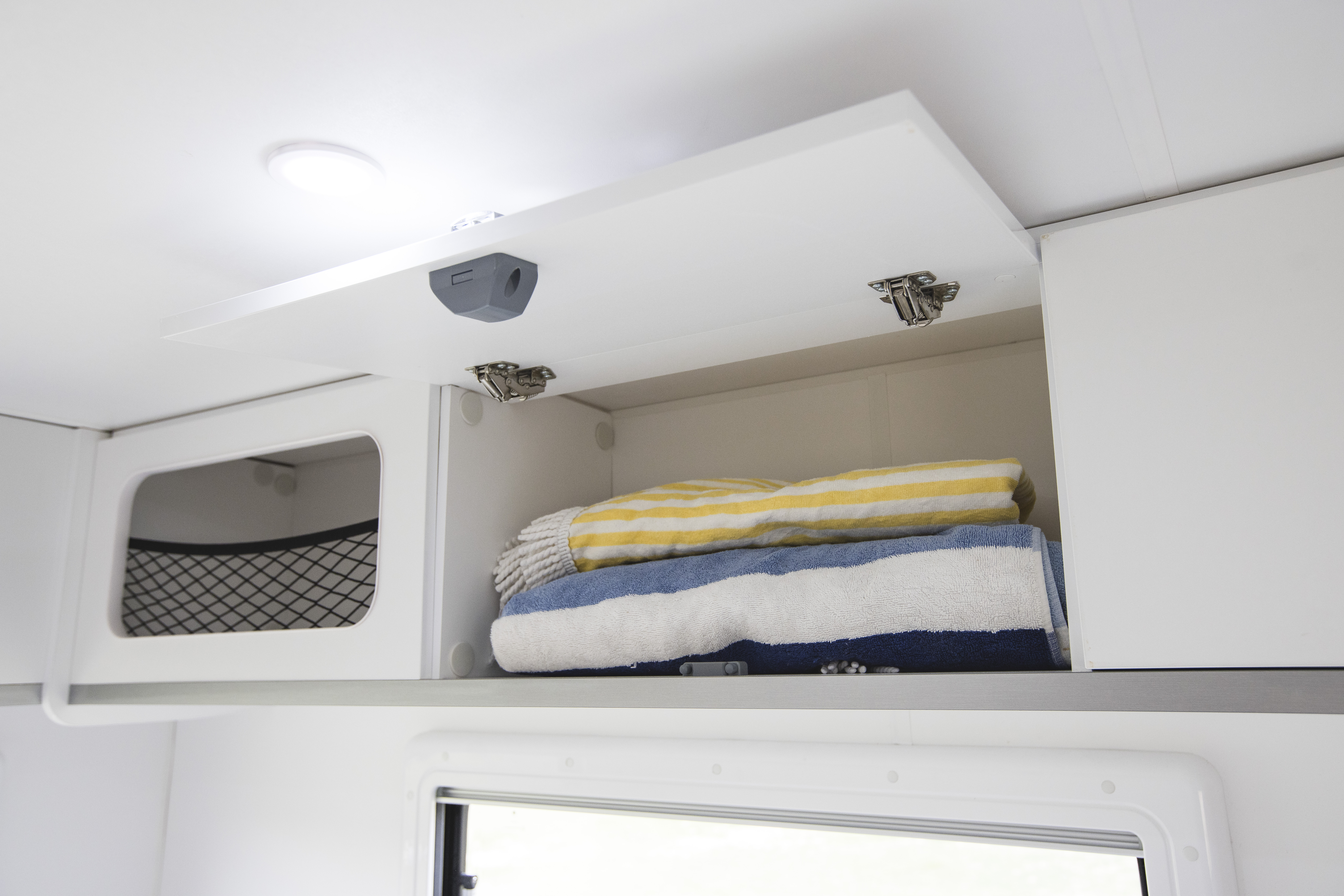 Open white overhead cabinet in campervan with folded striped towels inside.