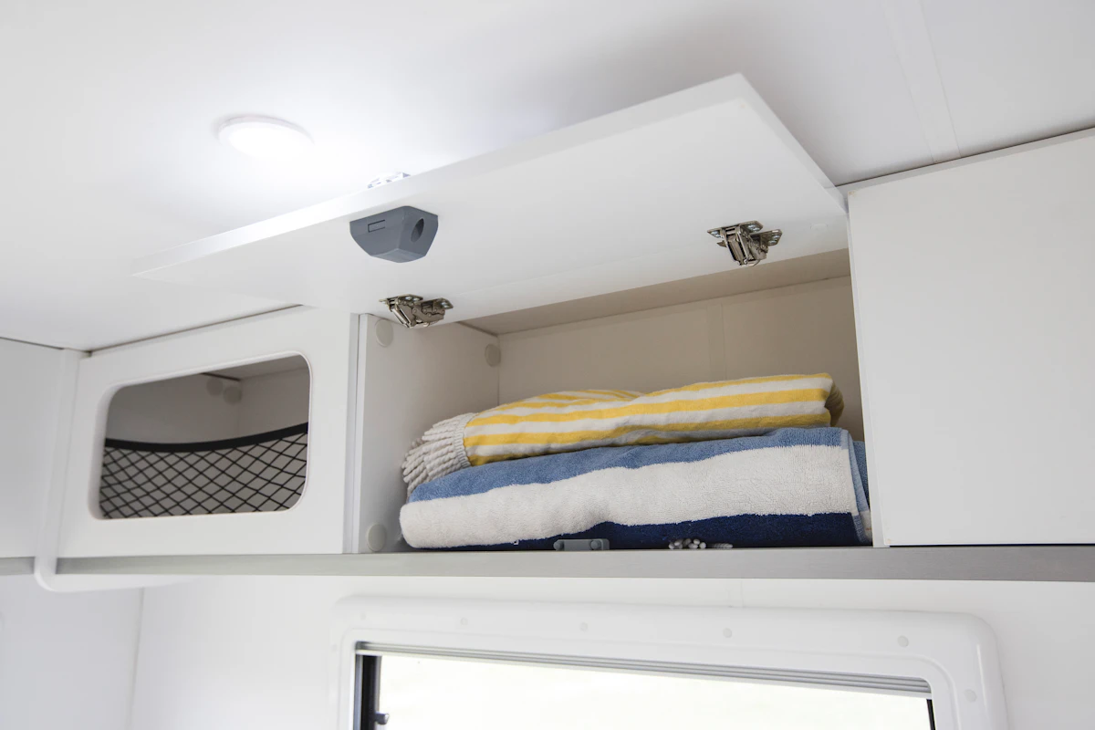 Open white overhead cabinet in campervan with folded striped towels inside.