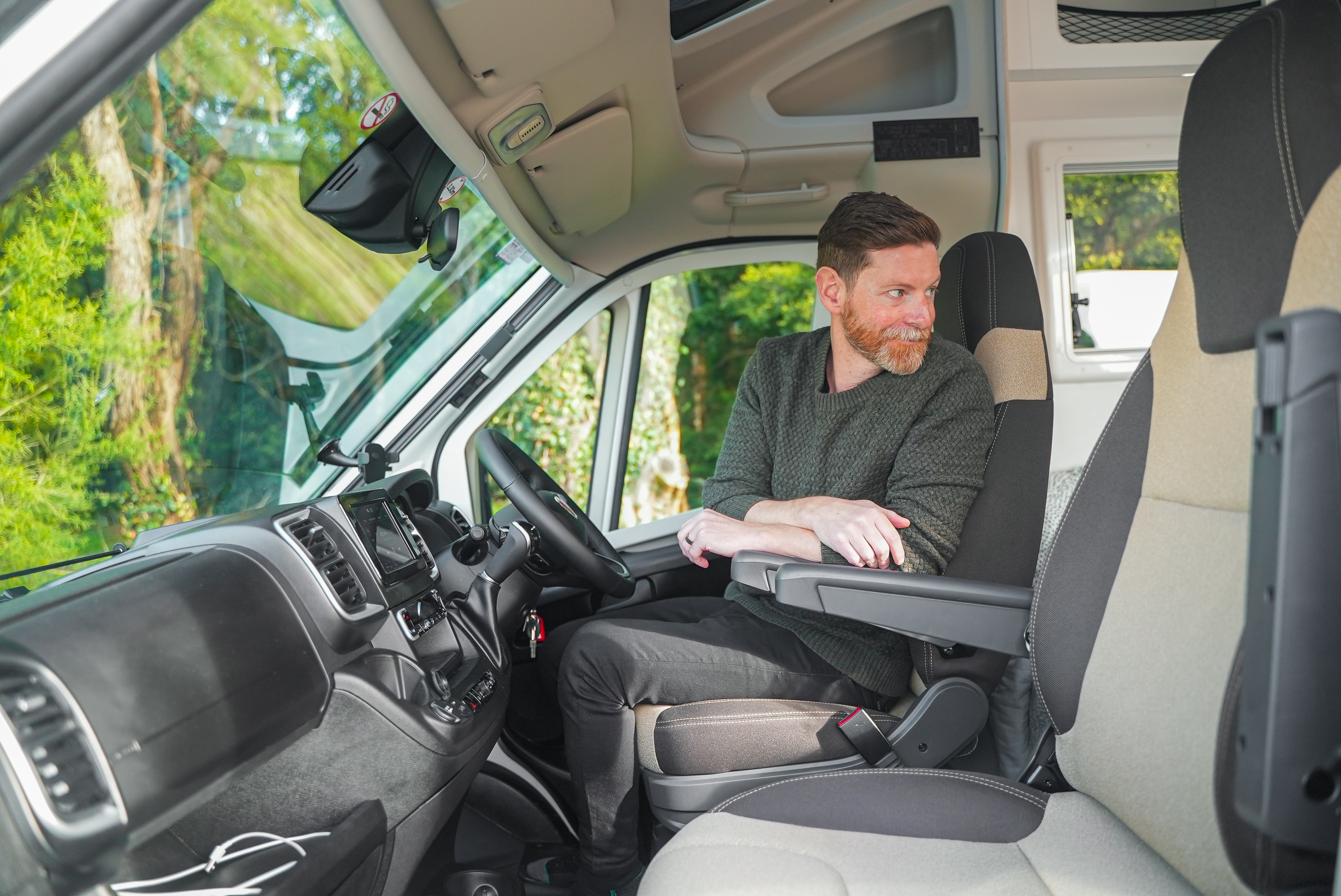 Man sitting in the driver's seat of a campervan, looking towards the back, interior view.