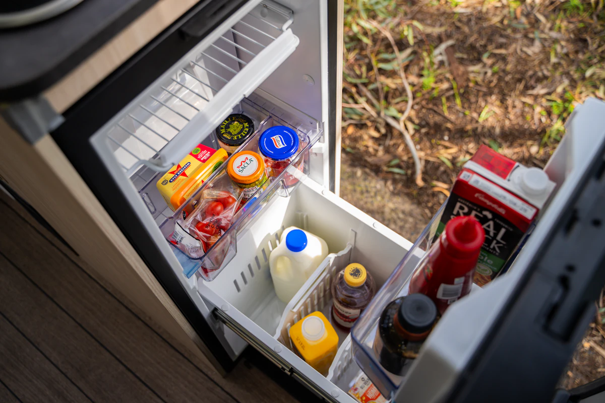 Small campervan fridge stocked with groceries including milk, juice, cheese, eggs, and condiments, viewed from above.