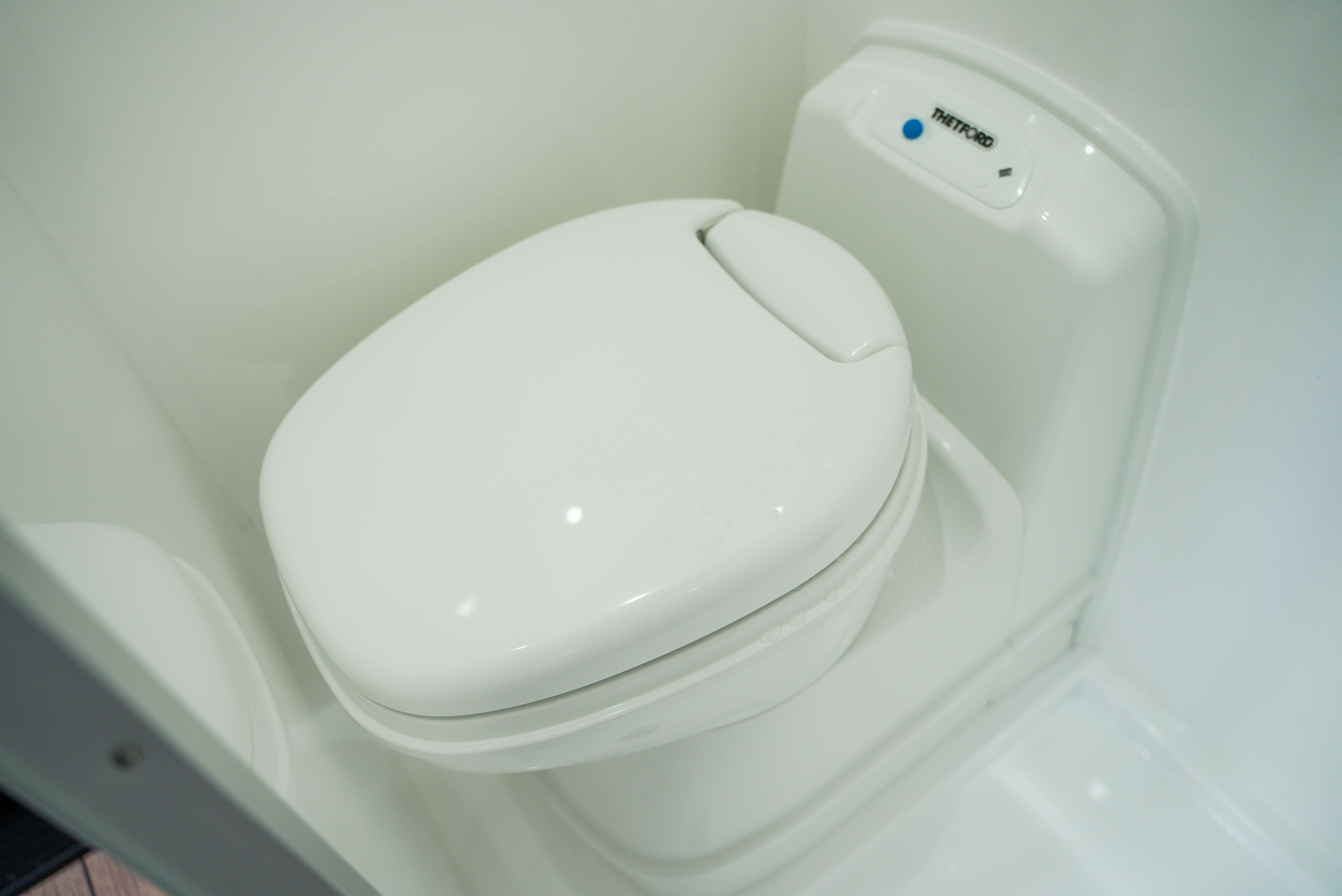 White compact campervan portable toilet with closed lid and flush button.