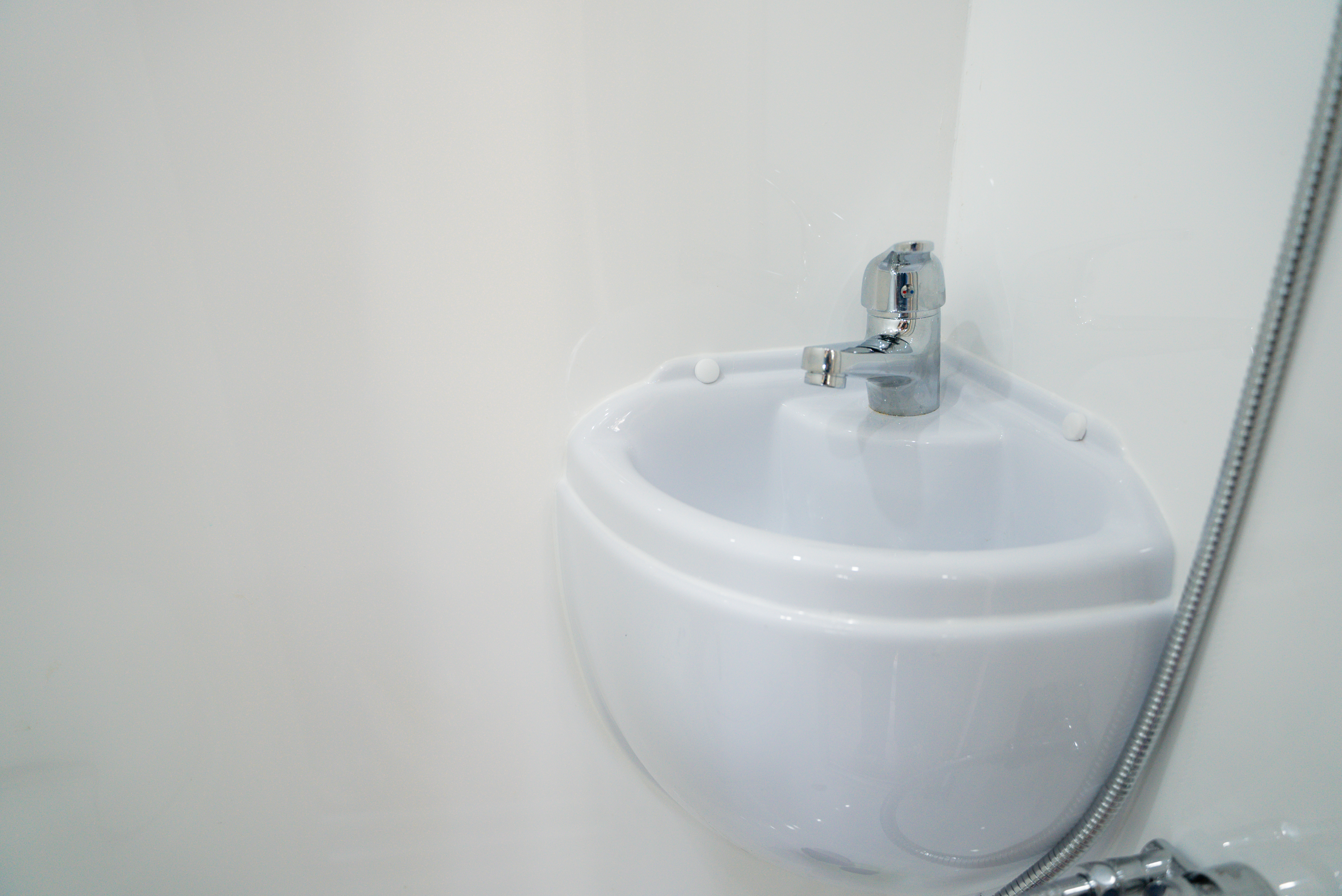 Compact white corner sink with a single lever chrome tap mounted on a white wall.