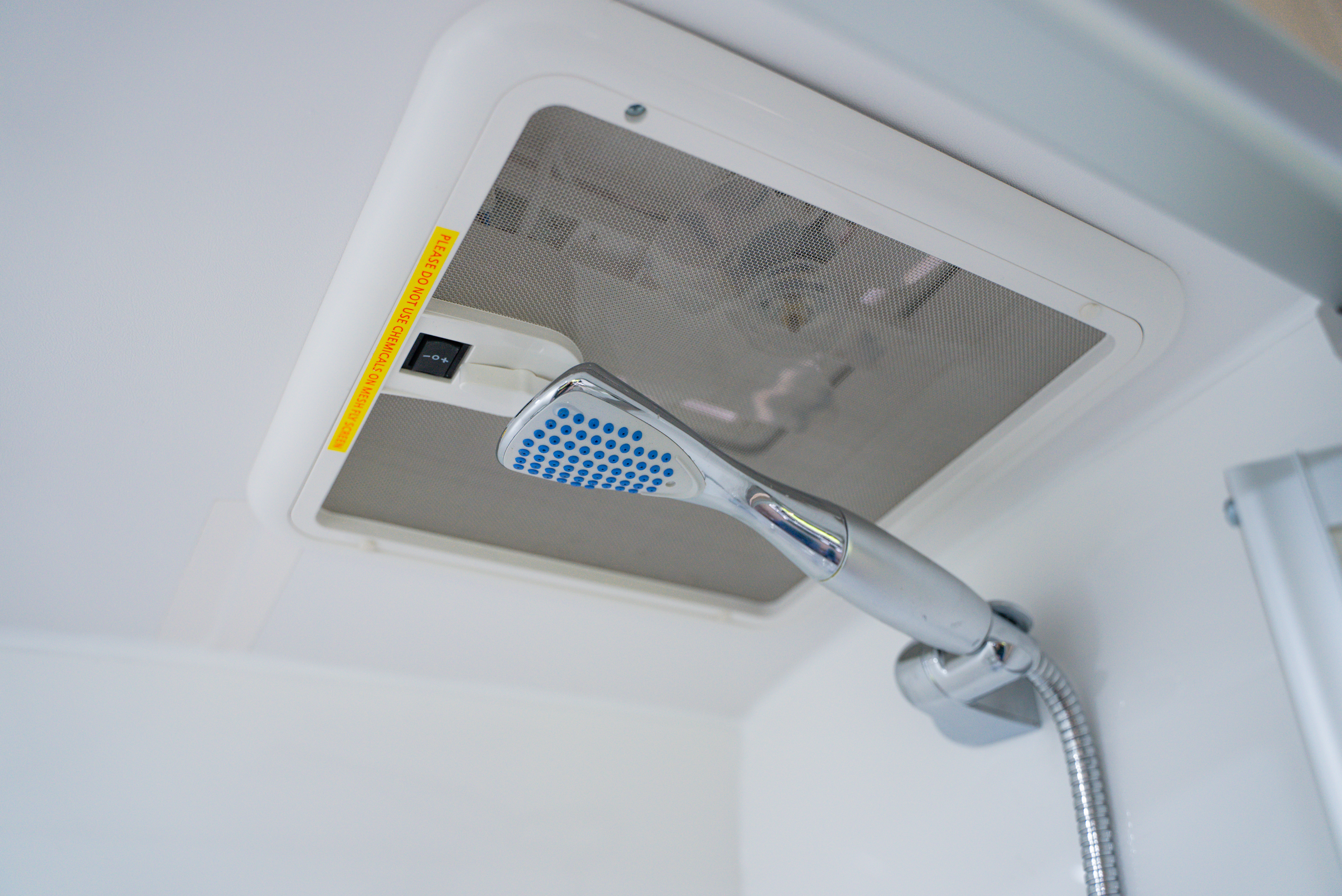 Close-up of a handheld showerhead mounted in a white shower cabin with a ventilation fan above.