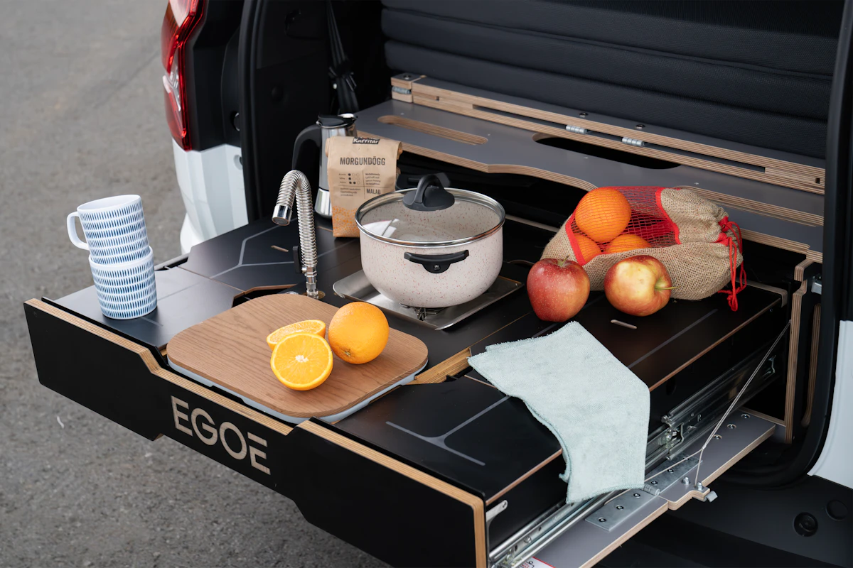 Pull-out camper kitchen with sink, pot, and fresh fruit displayed at the back of a van on a countertop.