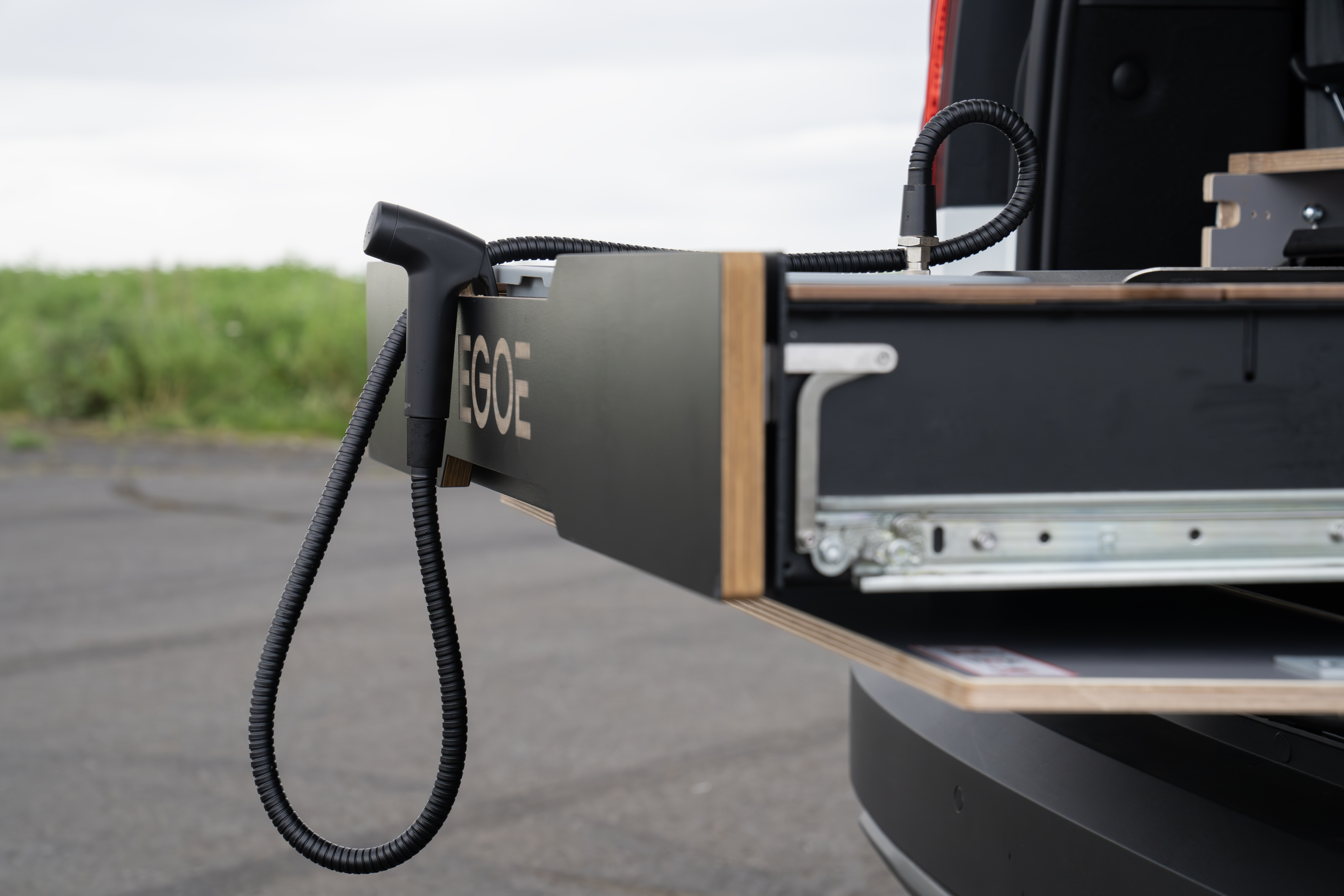 Camper van kitchen drawer with extendable countertop and attached hose, shown open at the rear of the vehicle.