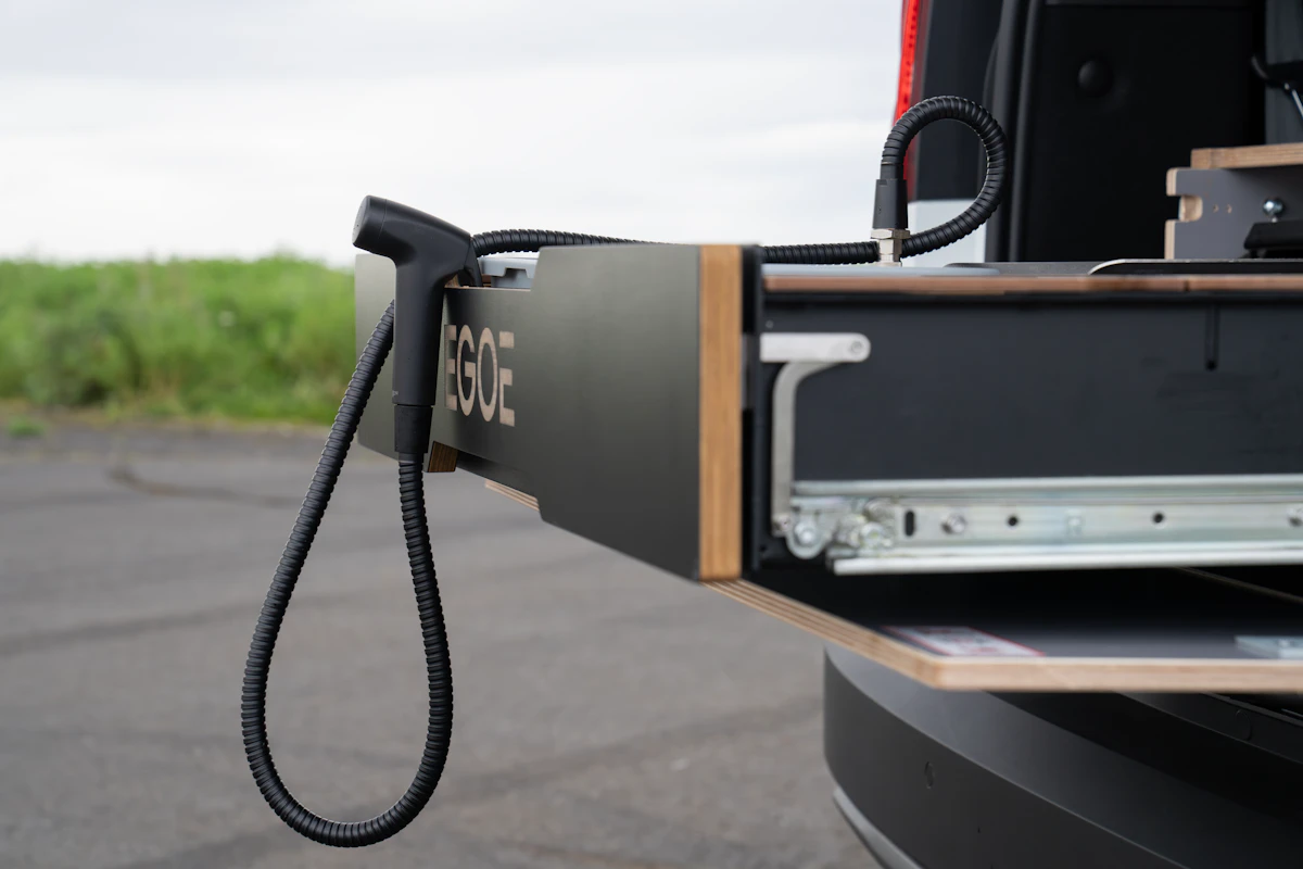 Camper van kitchen drawer with extendable countertop and attached hose, shown open at the rear of the vehicle.