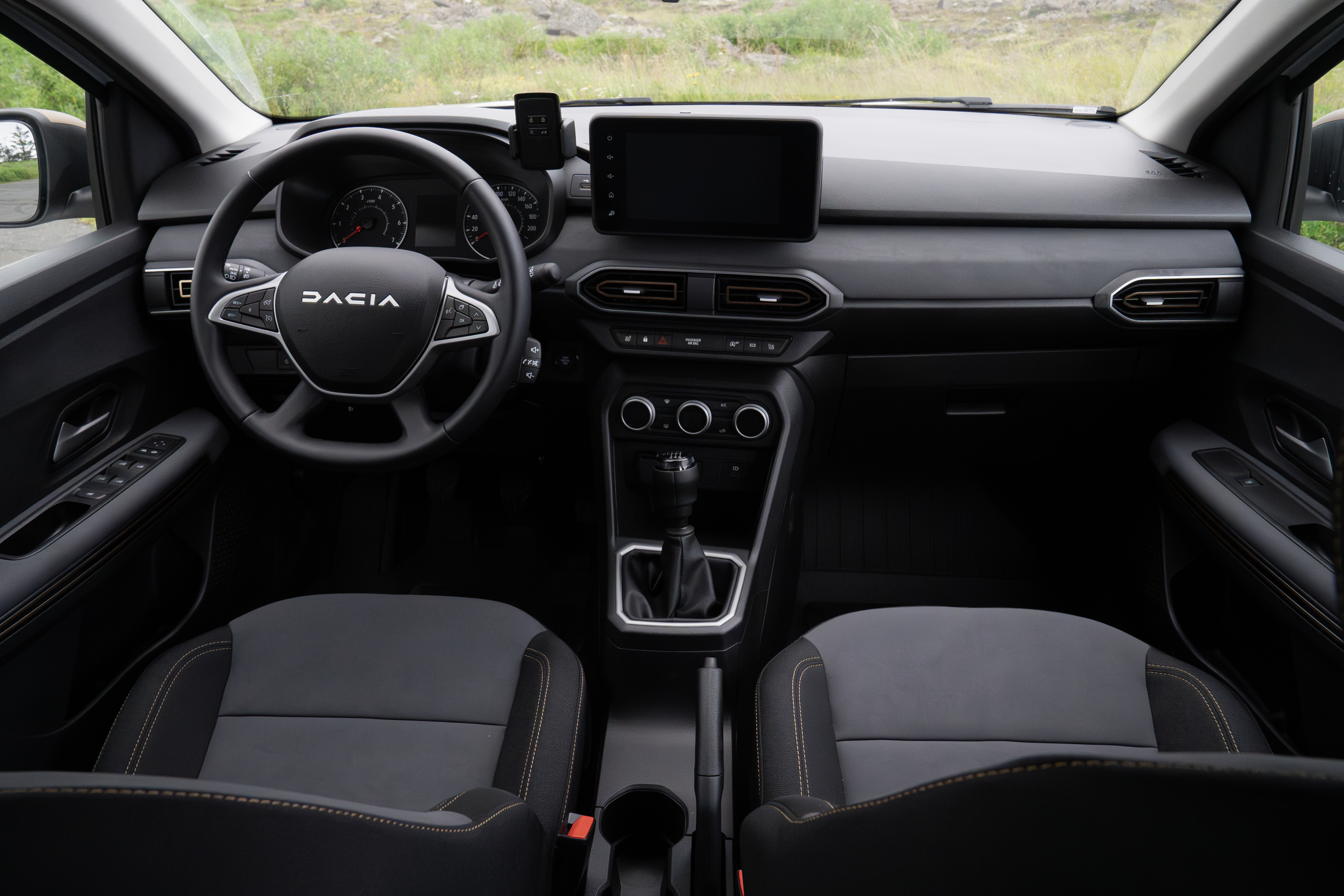 Modern Dacia car interior with touchscreen display, manual transmission, and black fabric seats, viewed from the front seats.