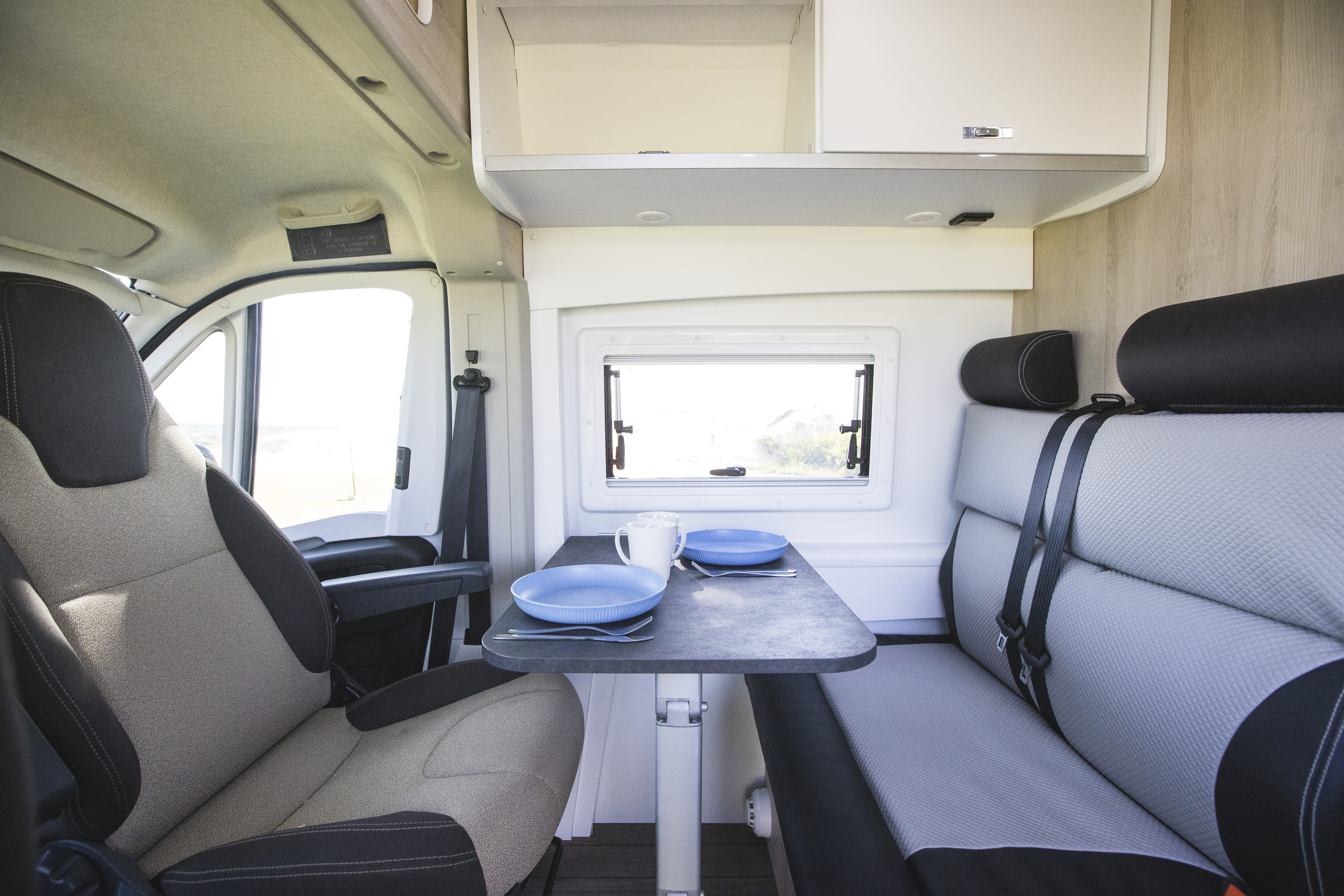 Modern campervan interior with a dining table, two blue plates, bench seating, and window, ideal for travel.