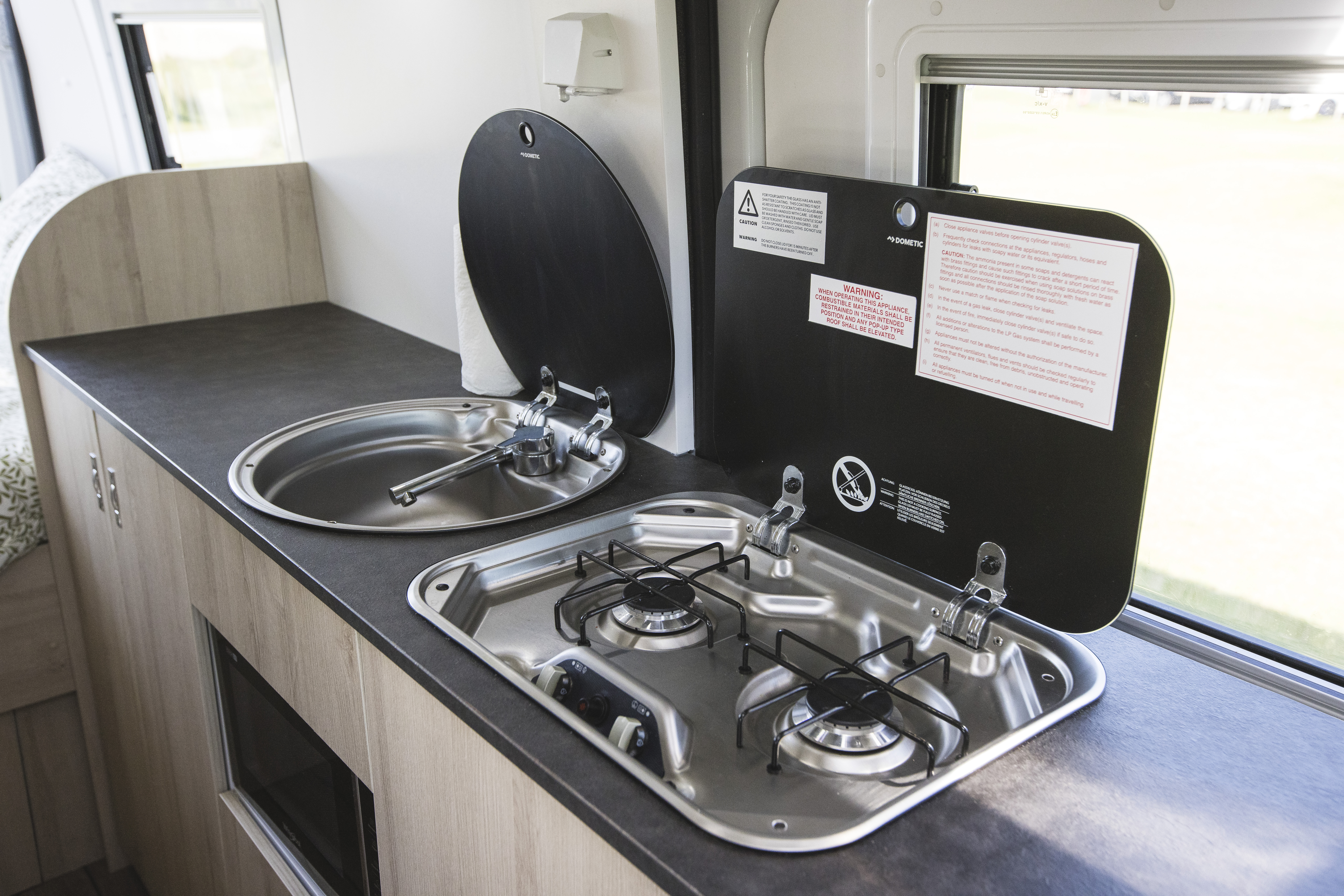 Modern campervan kitchenette with stainless steel sink and two-burner gas stove, set on a dark countertop.