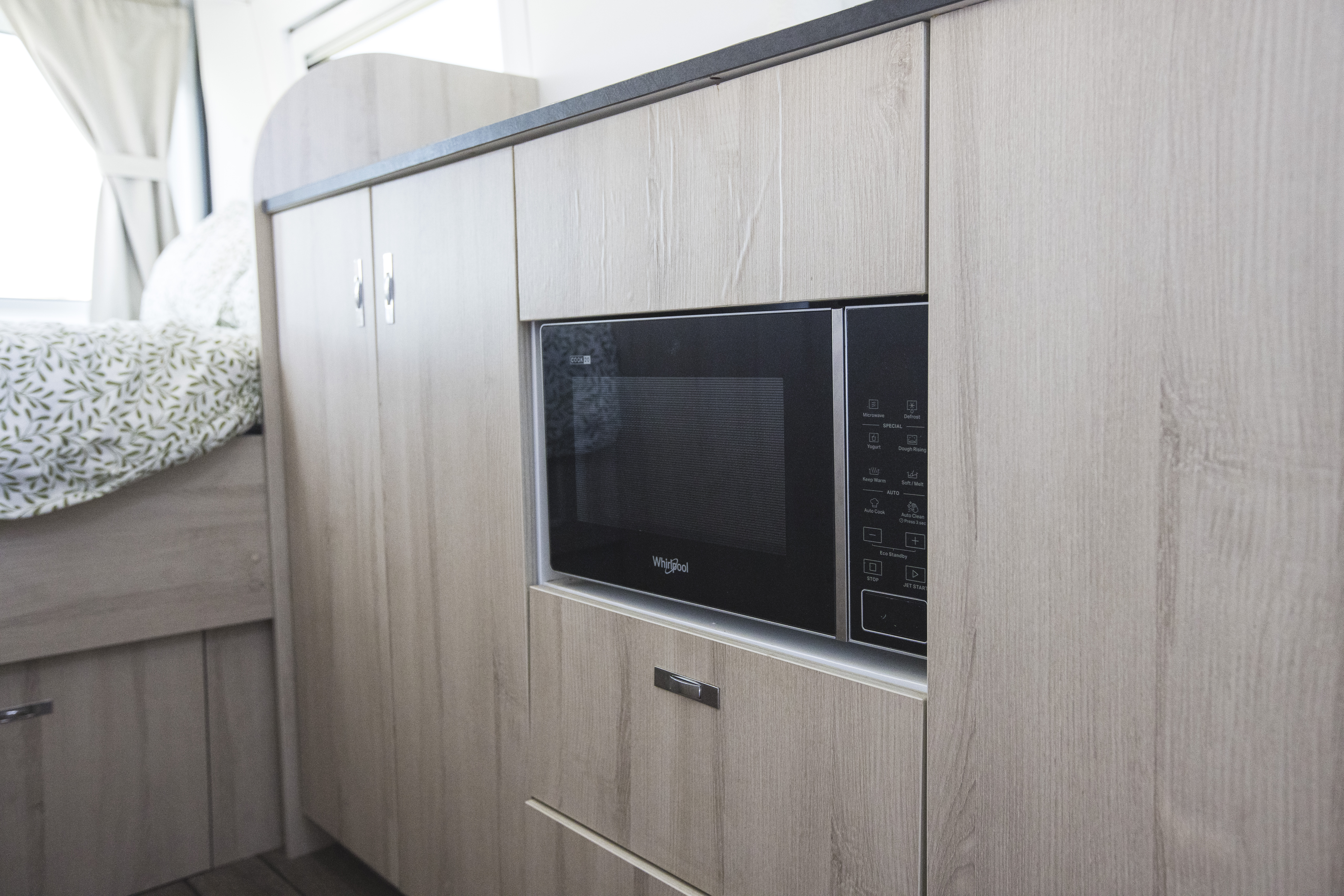 Built-in microwave oven set within light wood cabinetry inside the van kitchen area.