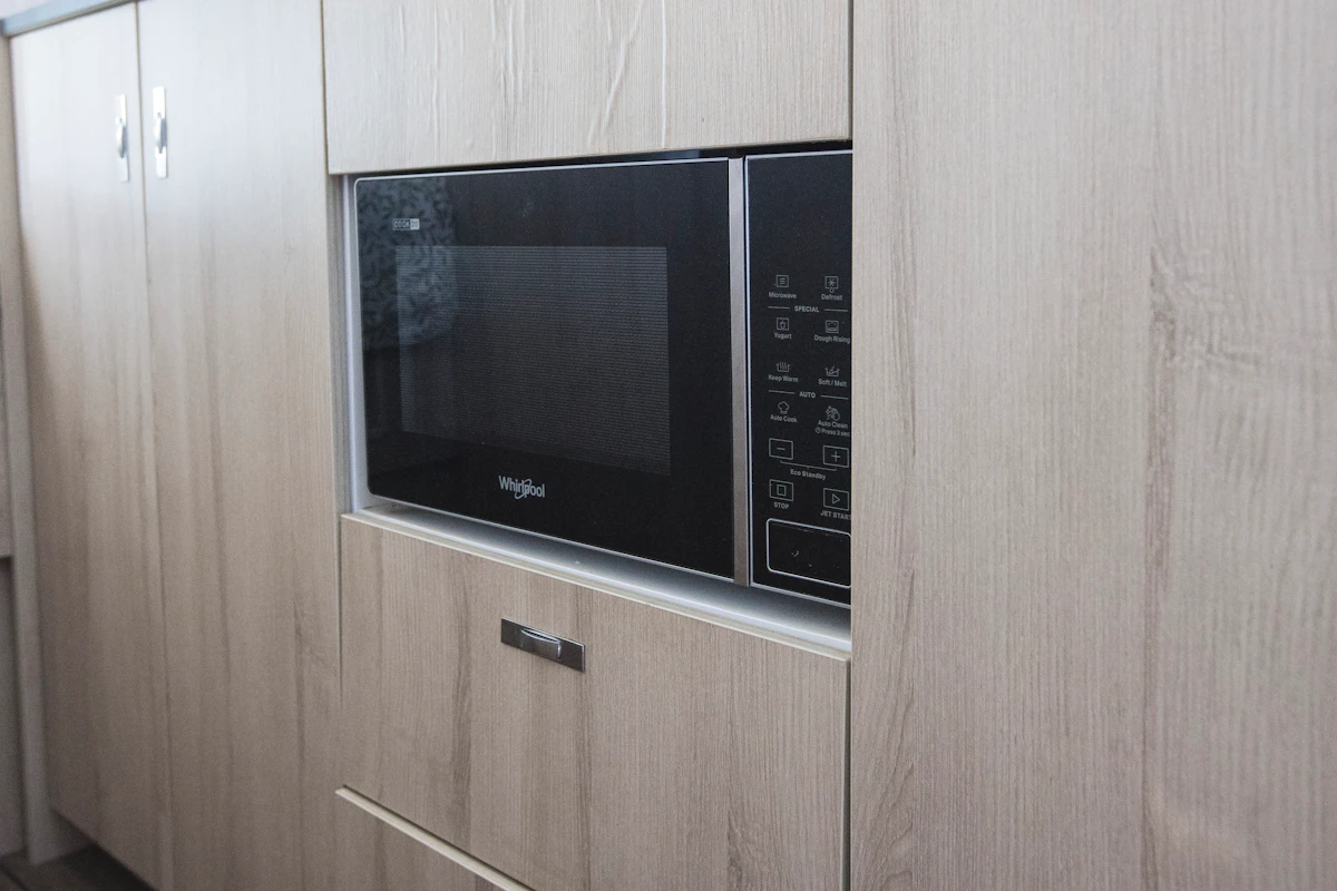 Built-in microwave oven set within light wood cabinetry inside the van kitchen area.