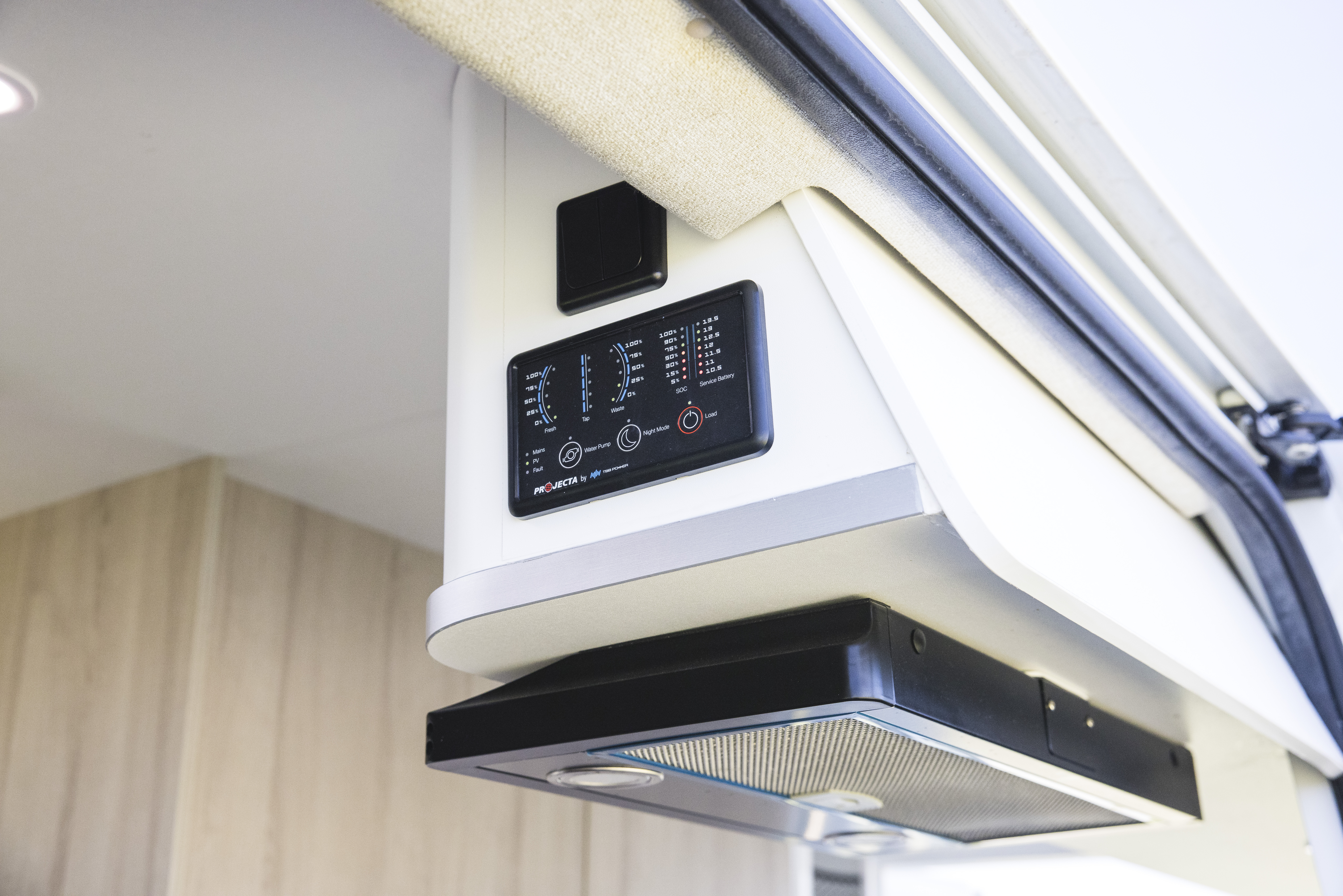 Campervan interior control panel and ventilation hood, mounted above a light wood kitchen area, with modern design.