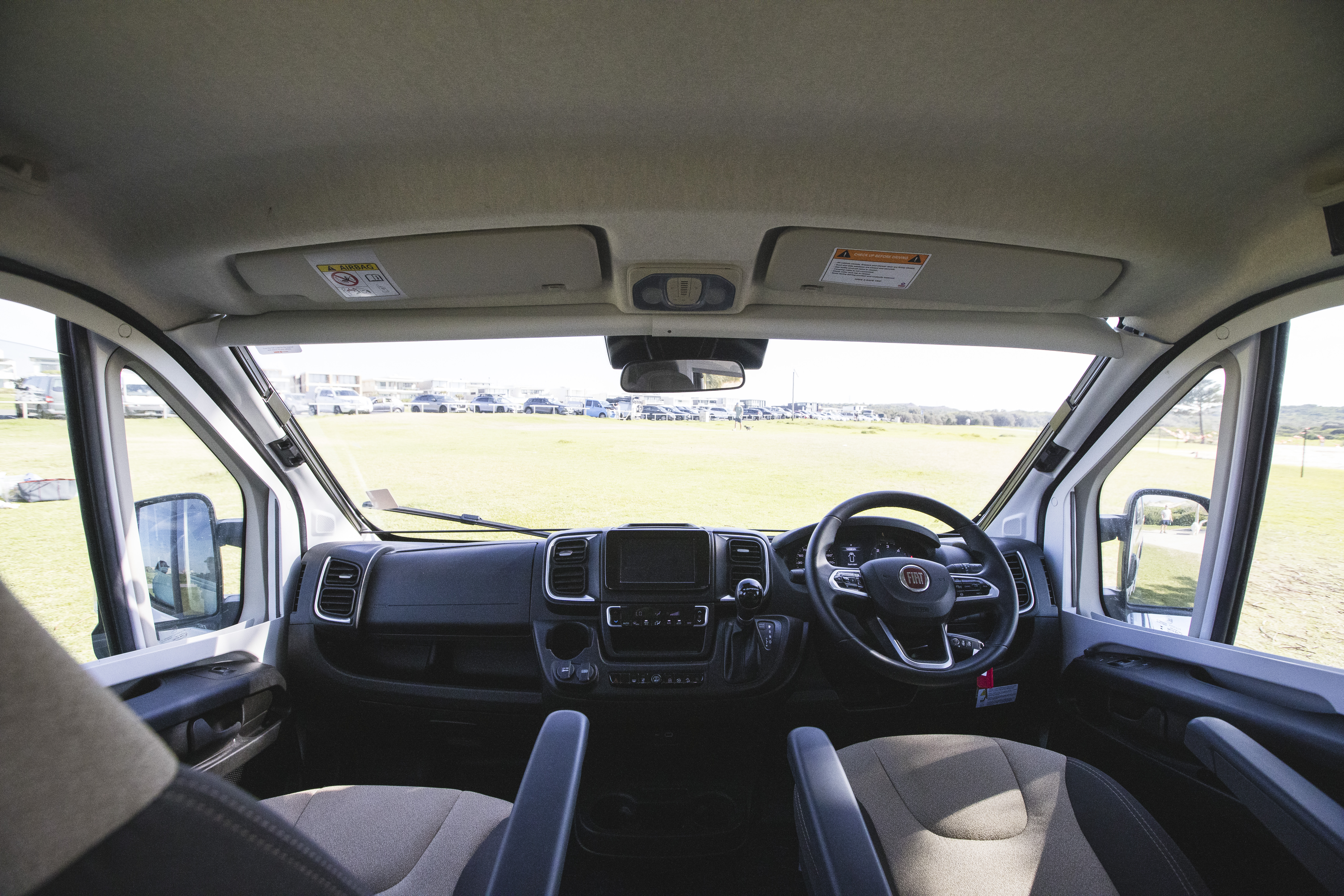 Interior view of a campervan cockpit with two seats and a scenic landscape visible through the windshield.