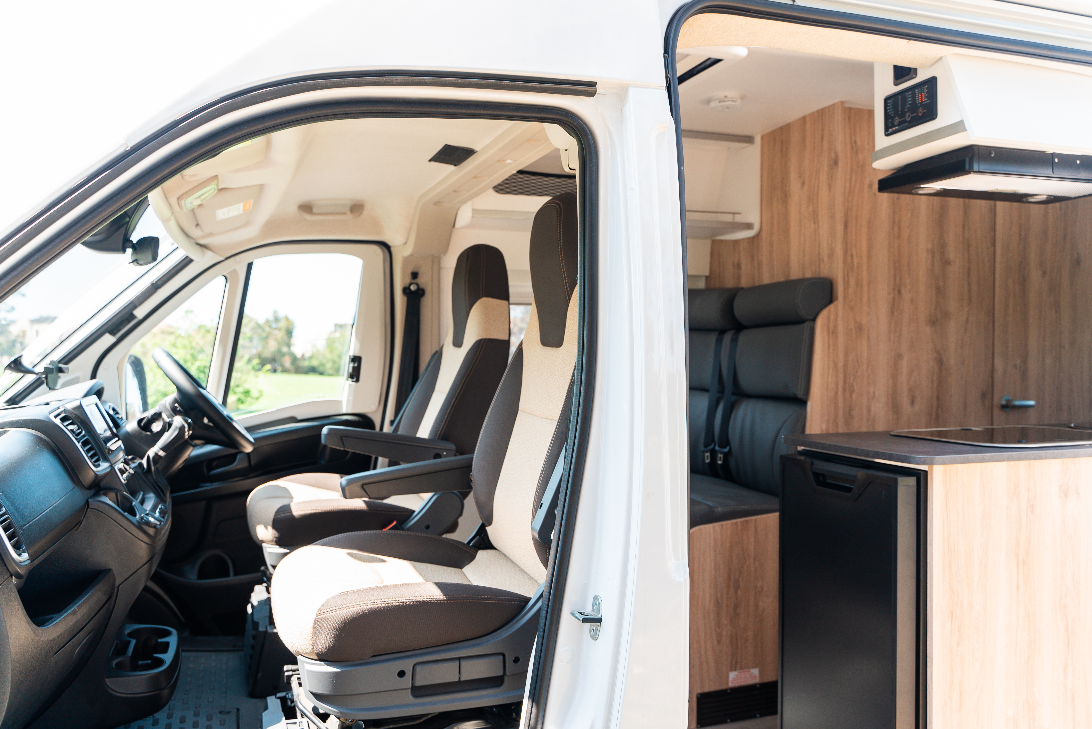 Interior view of a camper van showing driver seats, kitchenette with fridge, and a small seating area.