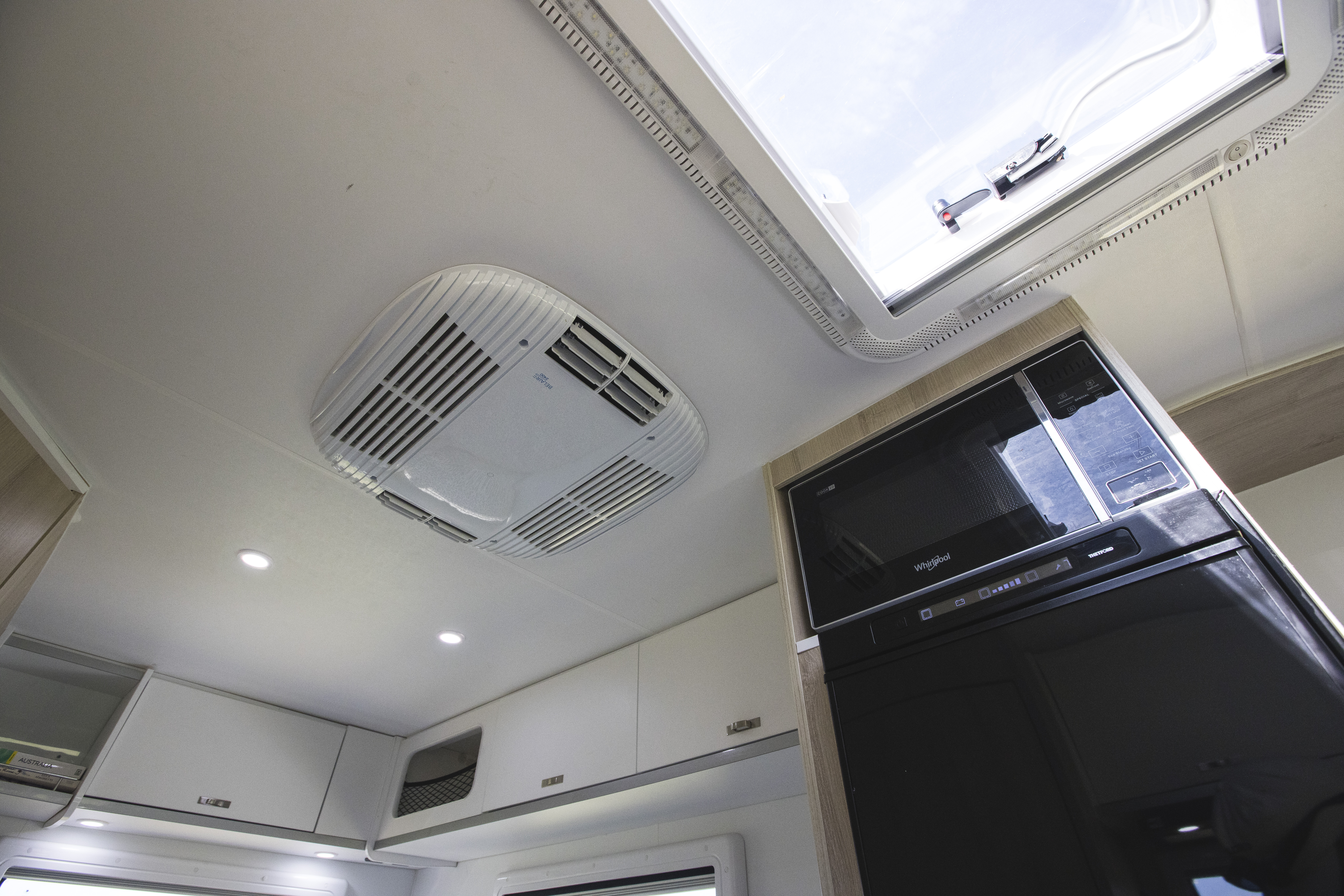 Interior campervan ceiling with built-in air conditioning unit, open skylight, modern cabinets, and black appliance.