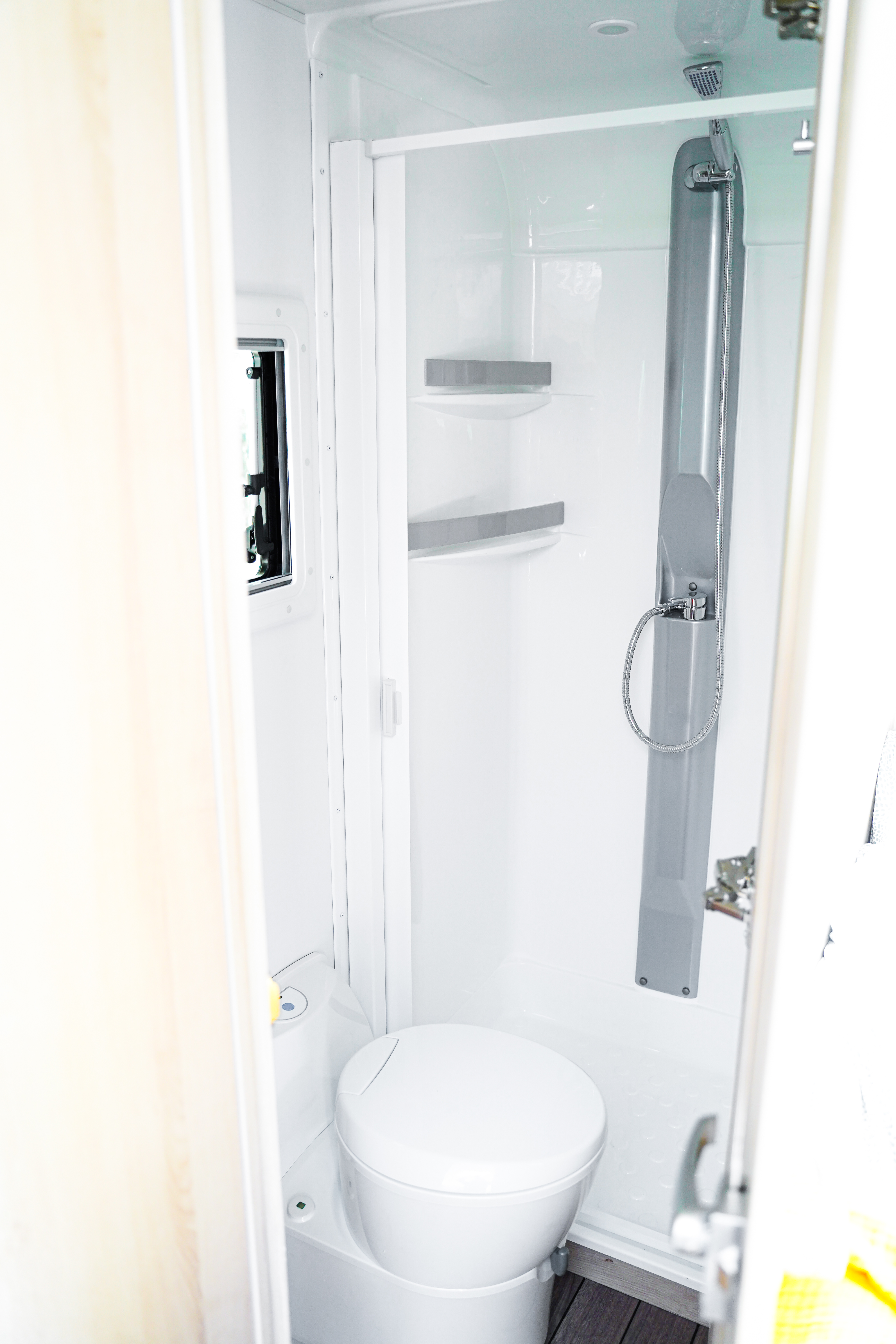 Compact white shower cabin with adjustable showerhead and small shelf inside a camper.