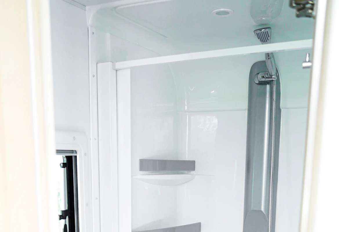 Compact white shower cabin with adjustable showerhead and small shelf inside a camper.