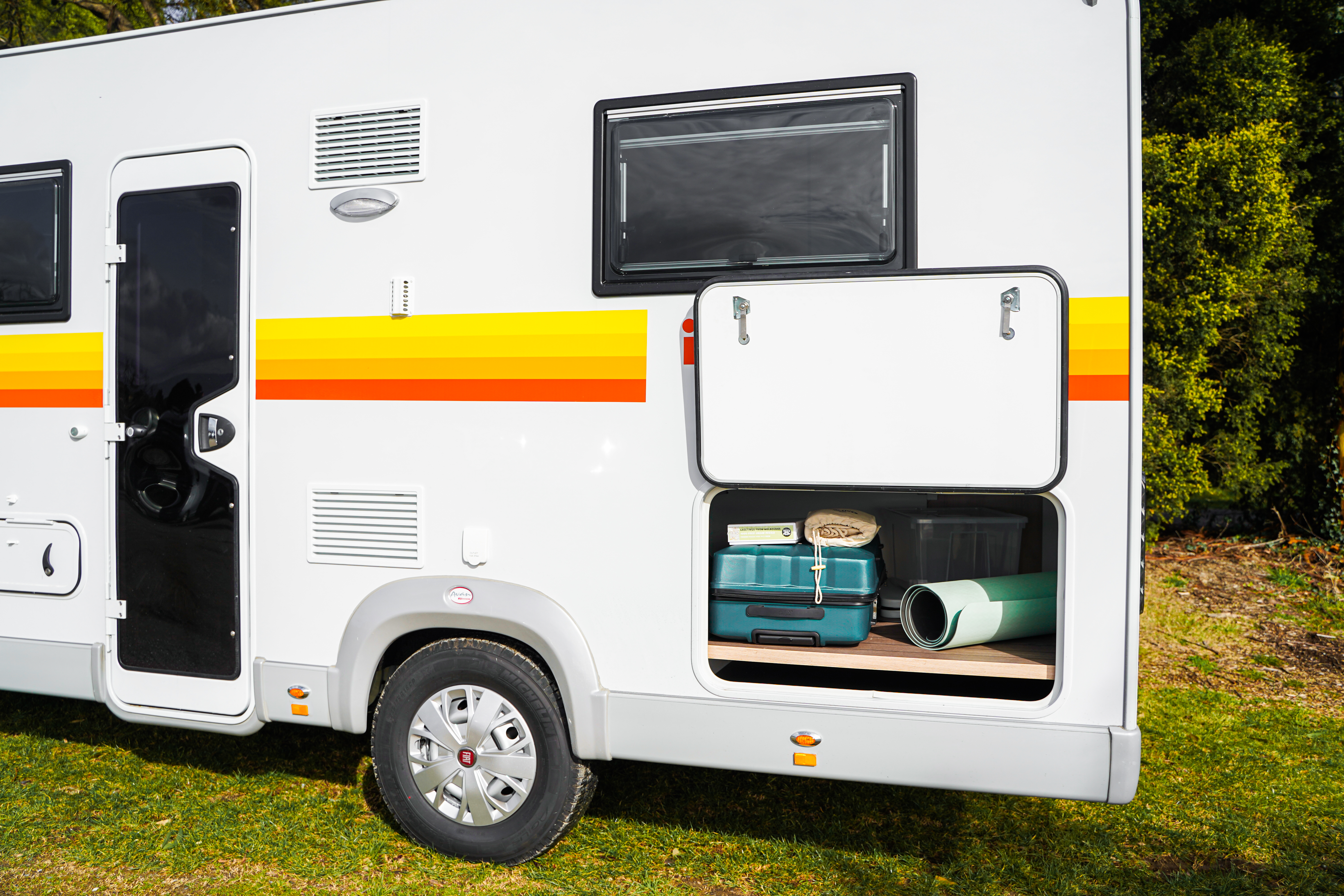 Side view of campervan with storage compartment open, showing camping gear and luggage inside, parked on grass.