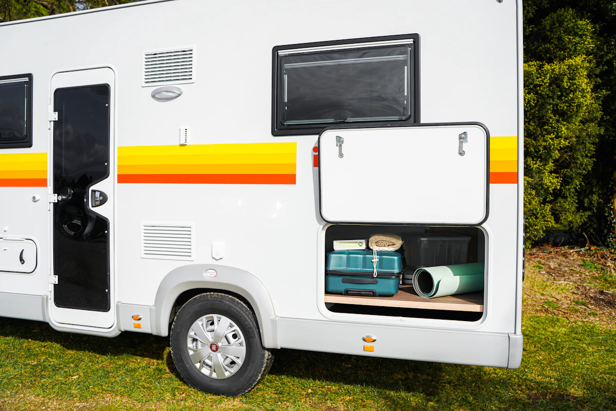 Side view of campervan with storage compartment open, showing camping gear and luggage inside, parked on grass.