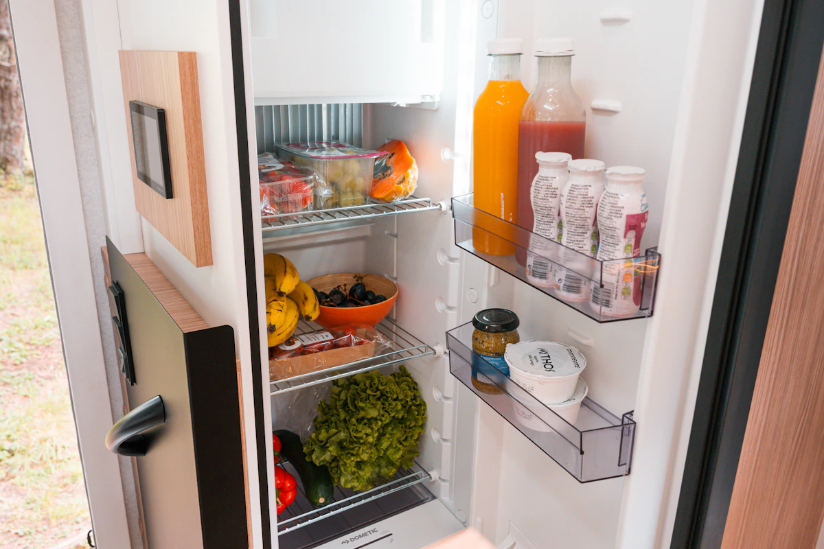 Open campervan refrigerator filled with fresh fruits, vegetables, juices, dairy products, and other groceries.