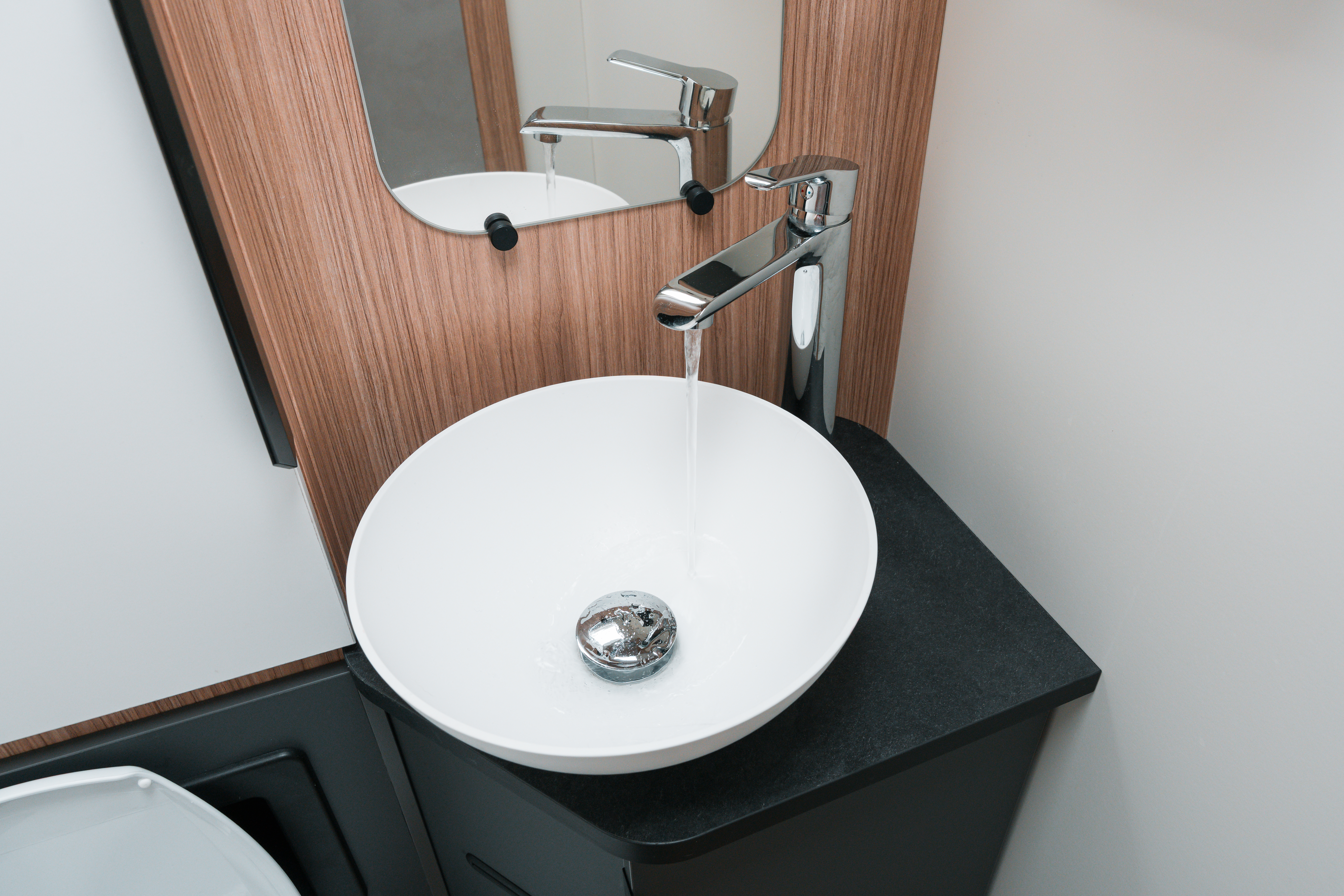 Modern campervan bathroom with a round white sink, chrome faucet, wooden paneling, and a mirror above.