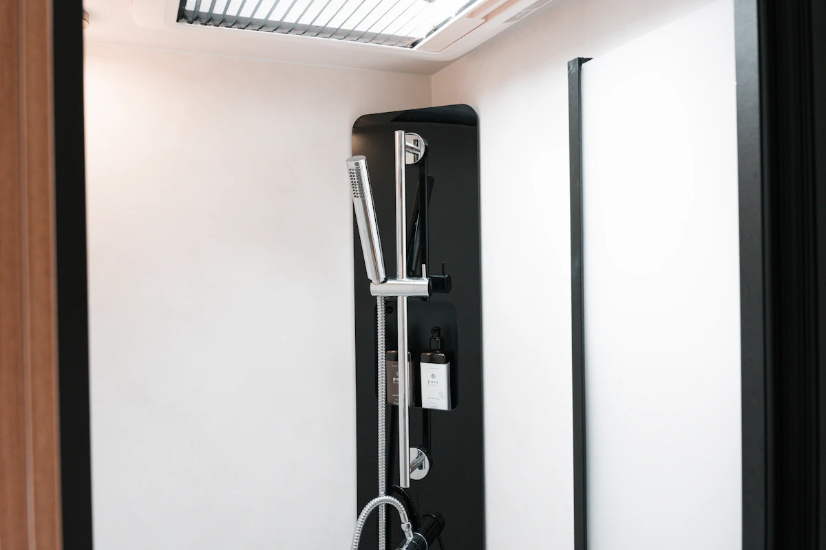 Modern campervan shower with black panel, detachable showerhead, and skylight, set against white walls.