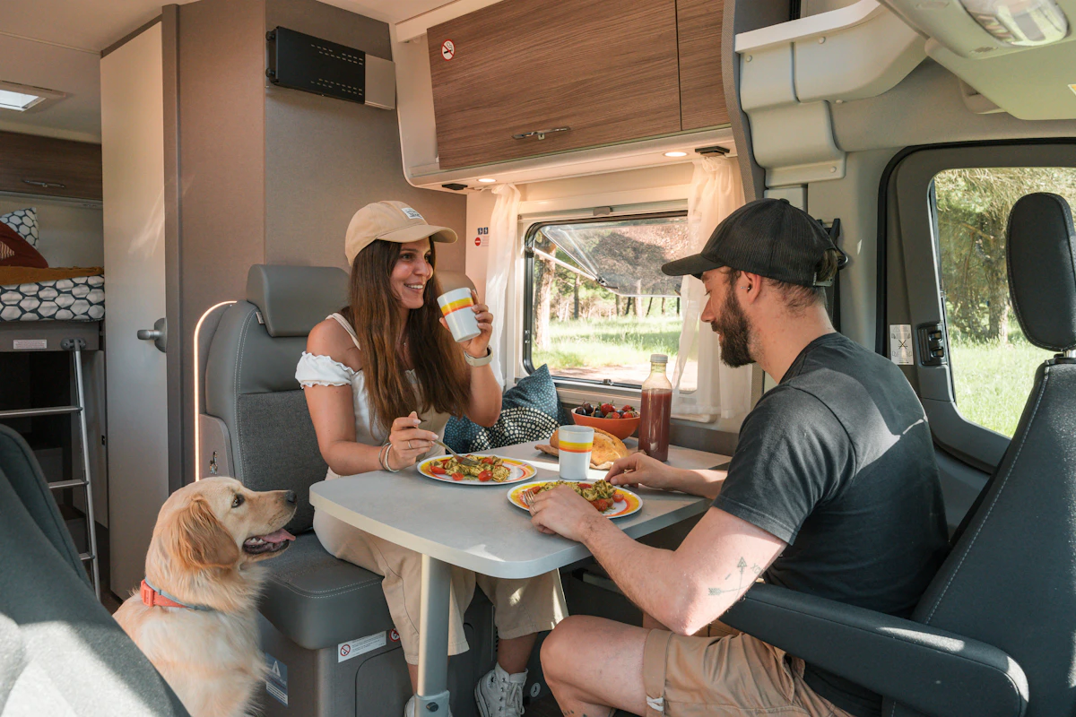 Paar genießt eine Mahlzeit im Wohnmobil mit ihrem Hund während einer Reise, natürliches Licht fällt durch das Fenster.
