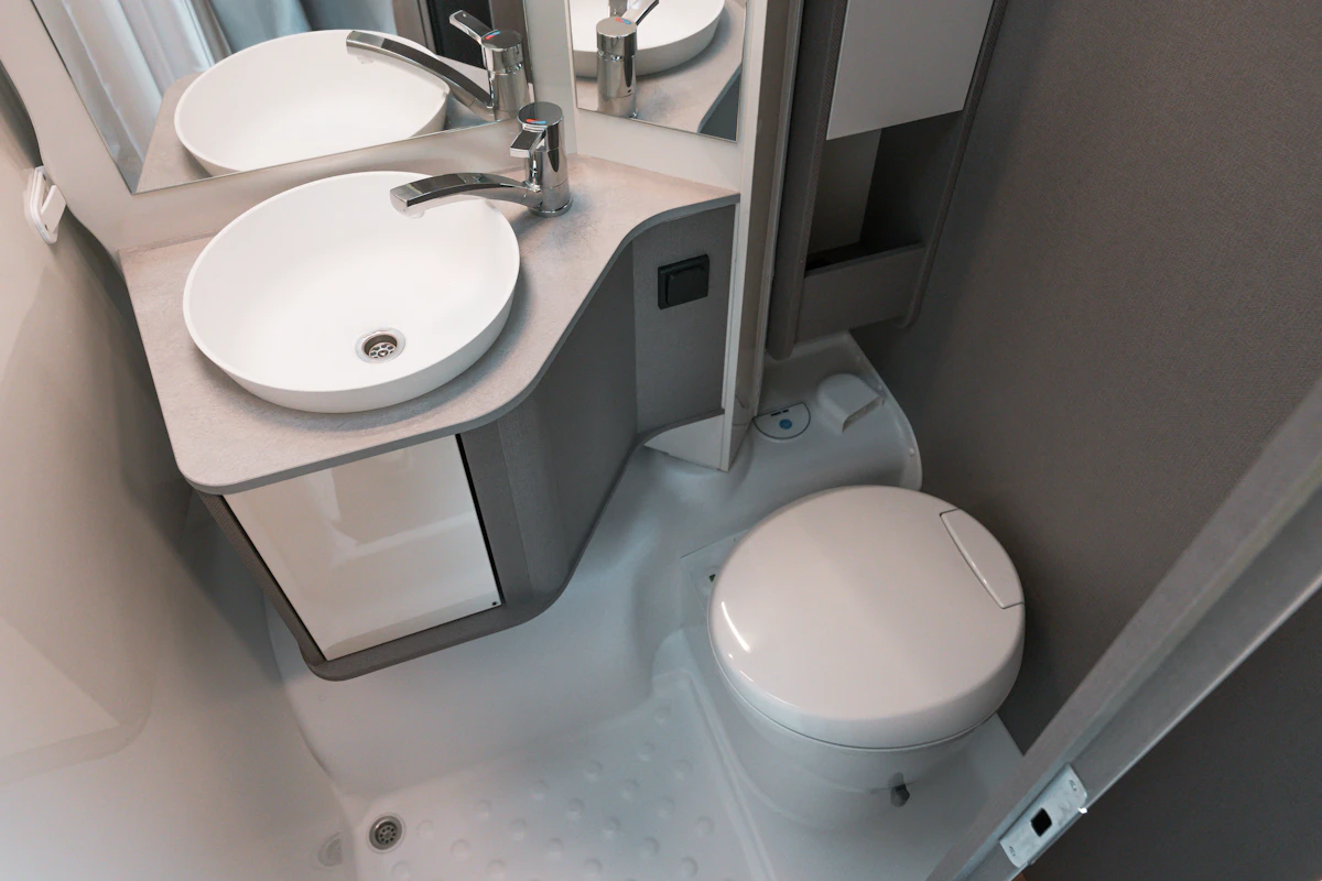 Modern campervan bathroom with a round sink, mirror, and compact toilet in a clean, white interior.
