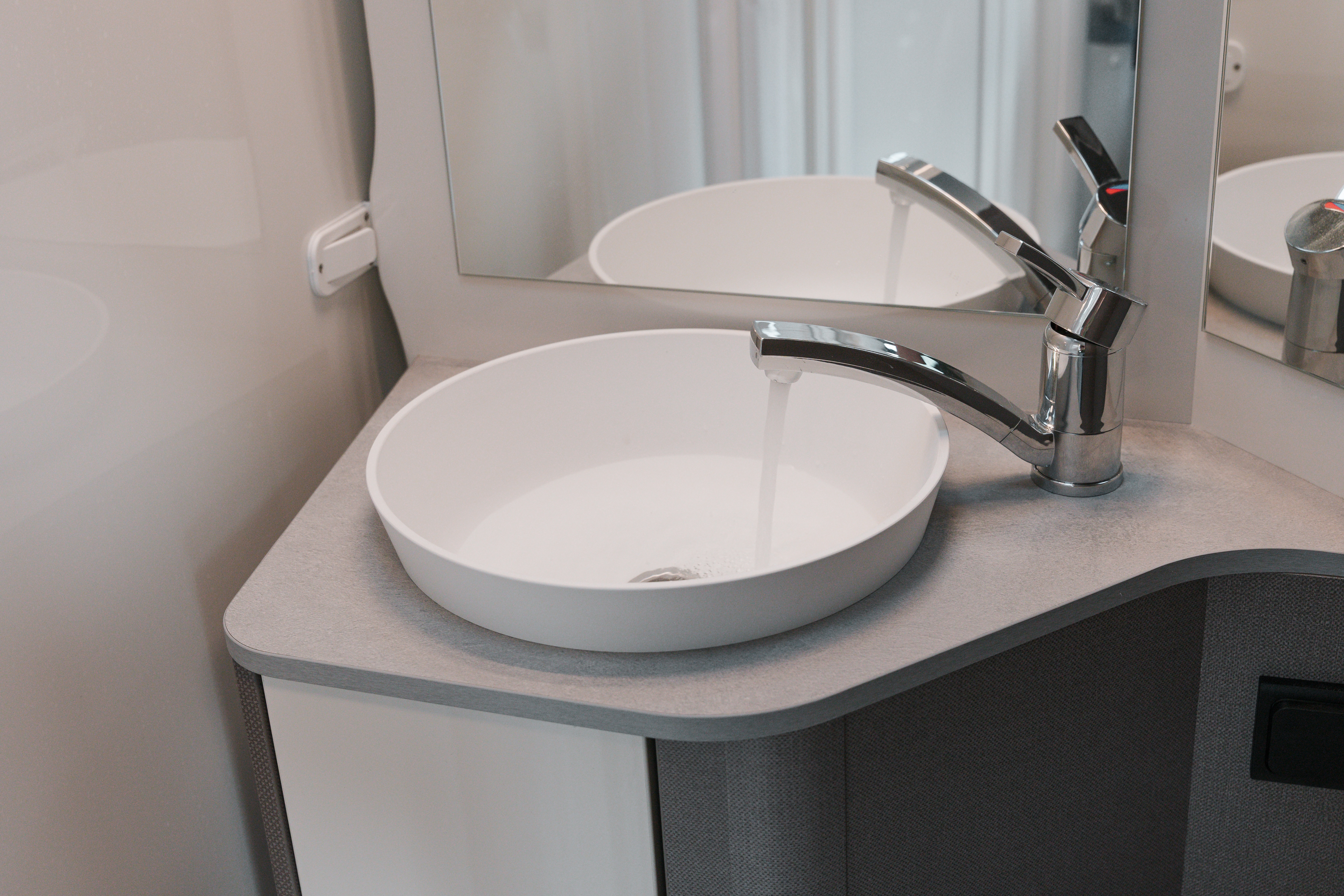 Modern campervan bathroom sink with running water, round basin, chrome faucet, and mirror on countertop.