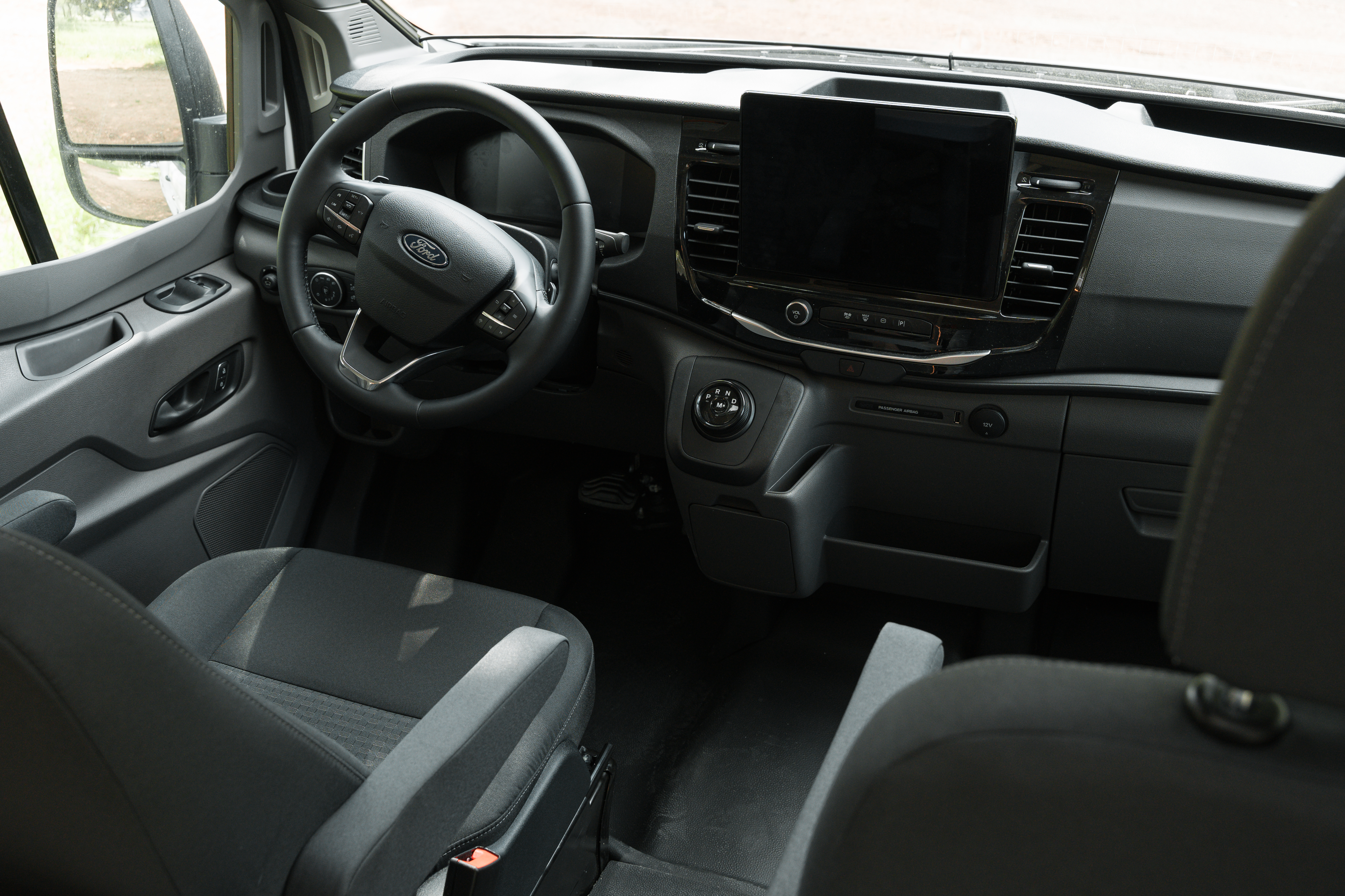 Modern camper van cockpit with steering wheel, large dashboard touchscreen, and two front seats in a bright interior.