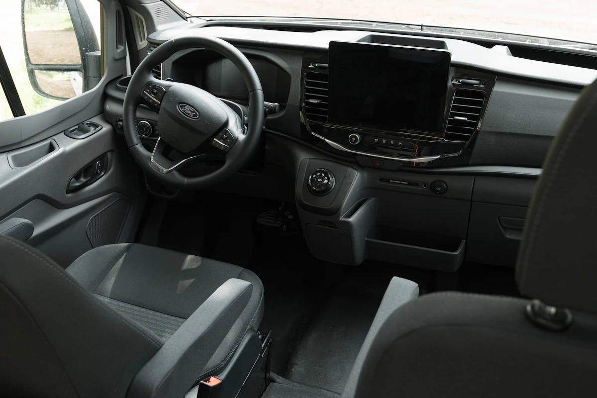 Modern camper van cockpit with steering wheel, large dashboard touchscreen, and two front seats in a bright interior.