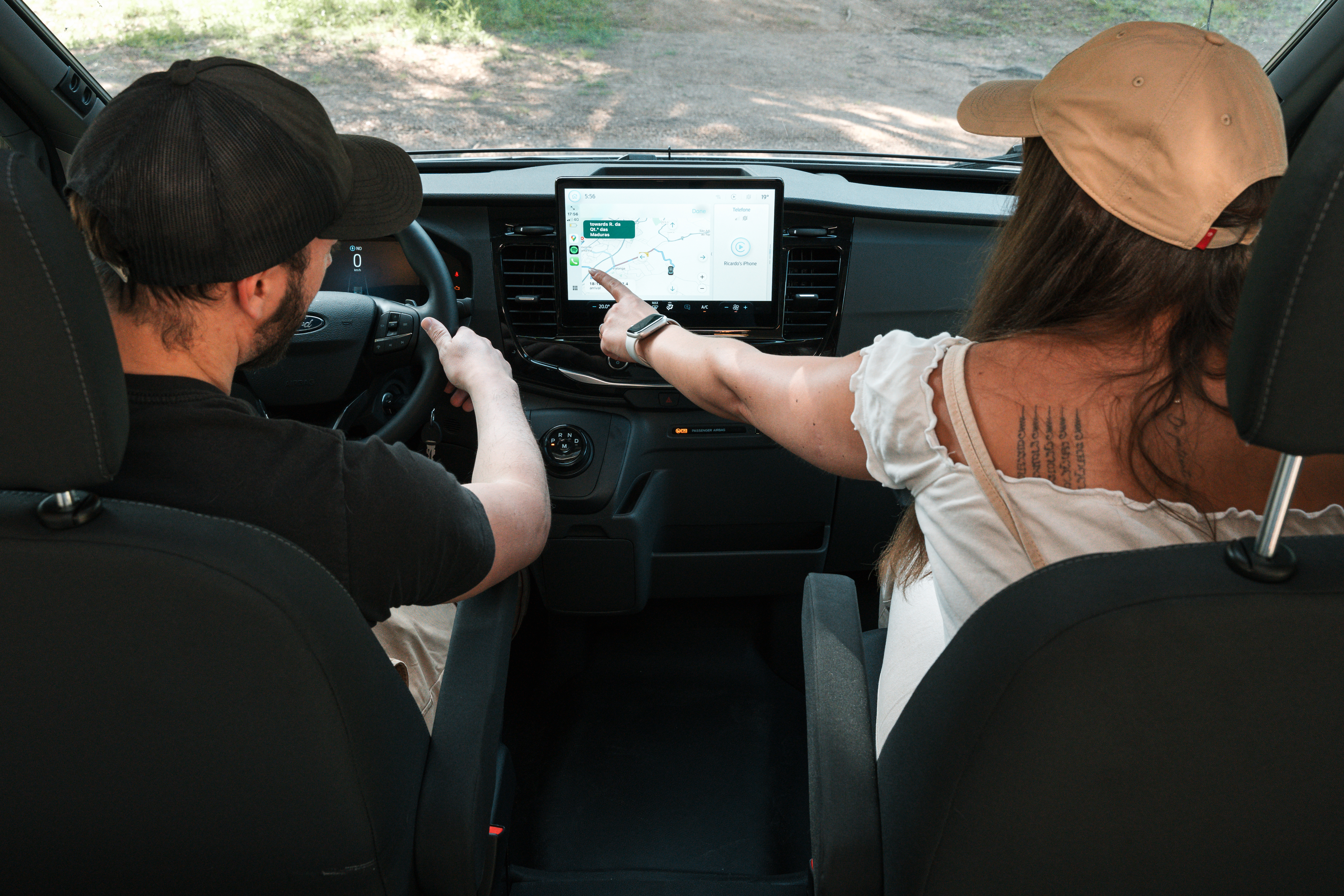 Two people sitting in a campervan, one driving and one pointing at the navigation screen on the dashboard.