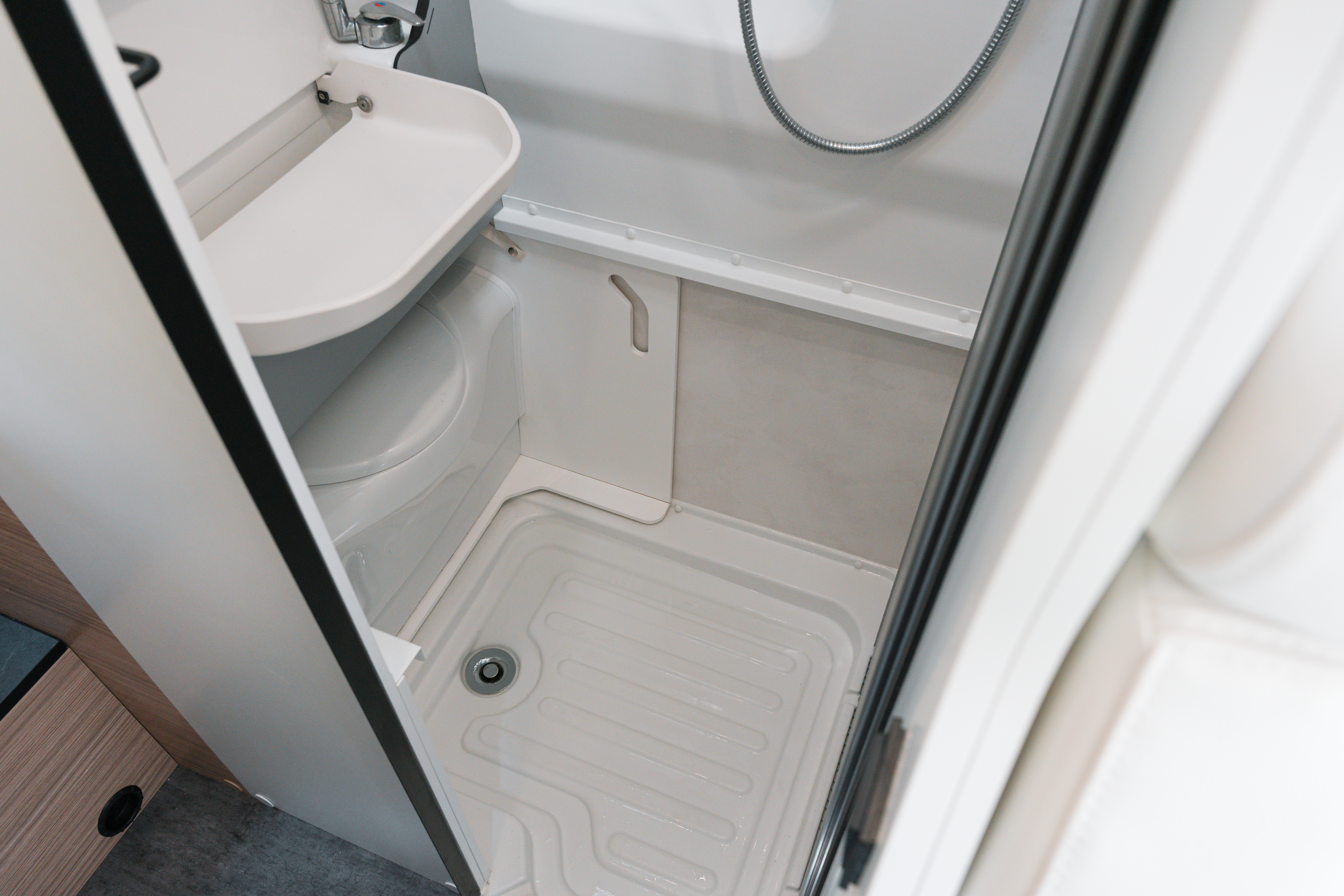 Compact campervan bathroom with integrated shower, toilet, and small sink, showcasing practical and modern interior design.