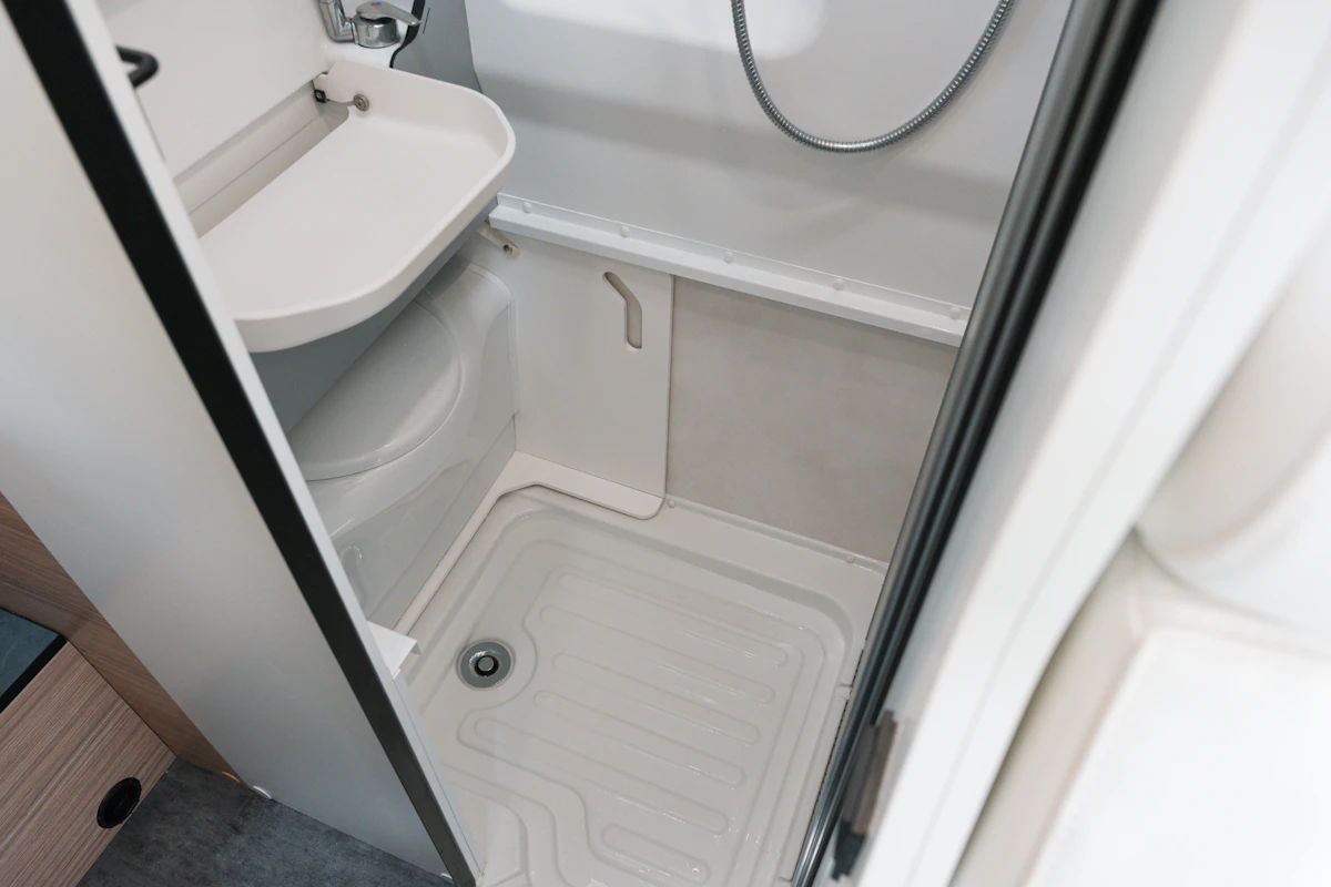 Compact campervan bathroom with integrated shower, toilet, and small sink, showcasing practical and modern interior design.