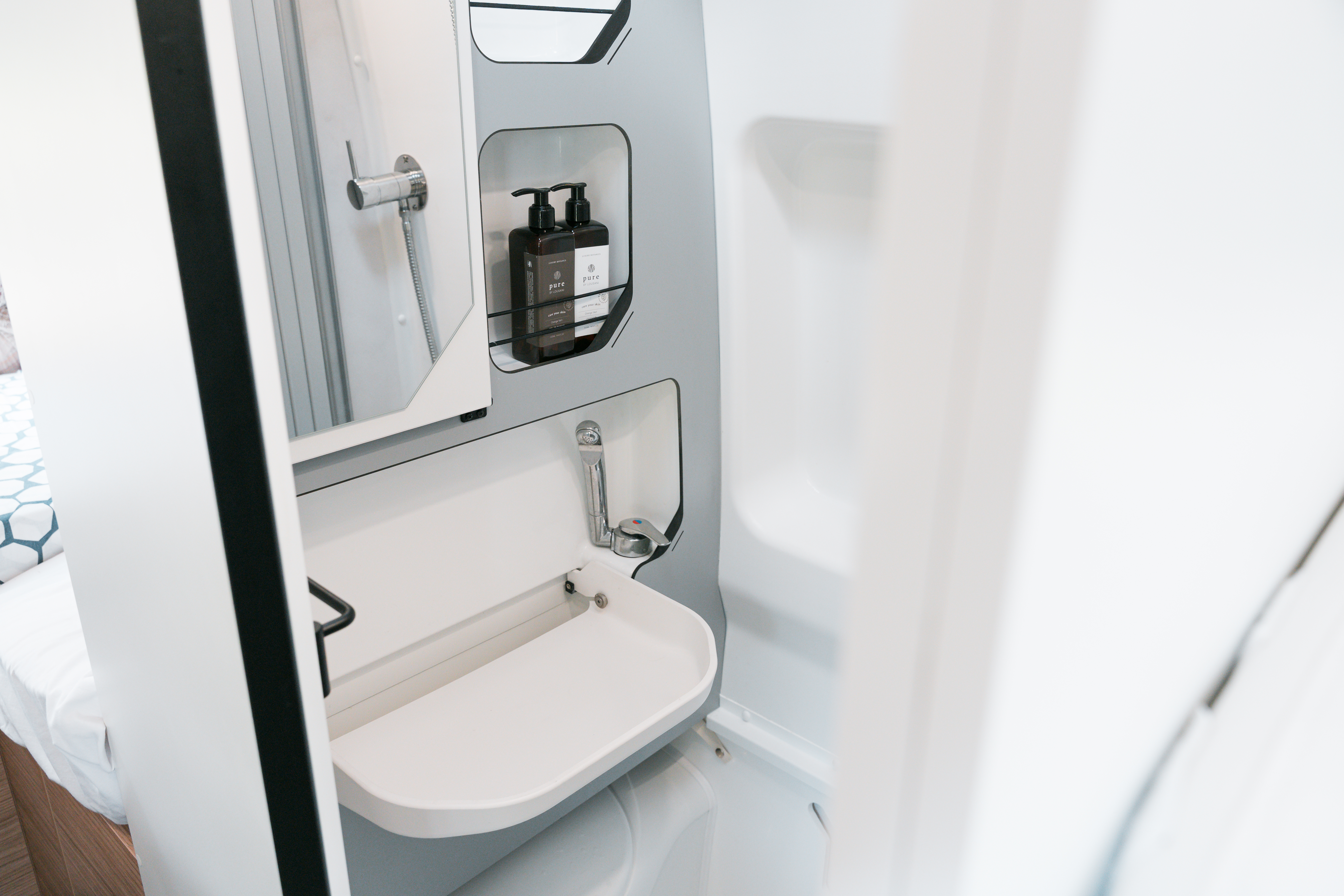 Modern campervan bathroom with compact sink, faucet, mirror, and toiletries shelf, showcasing efficient use of space.