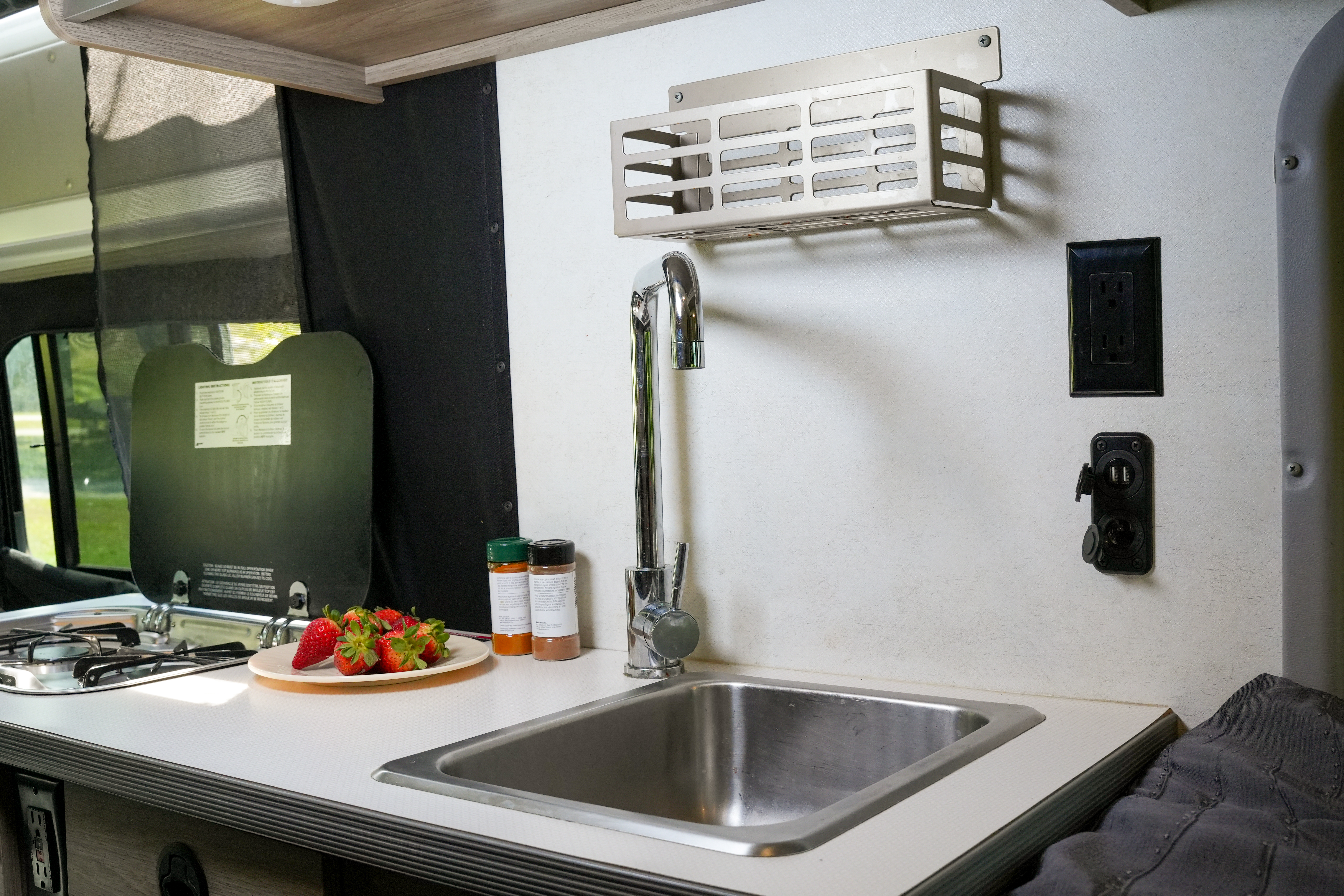 Compact van kitchen interior with sink, gas stove, and countertop featuring spices and a plate of strawberries.