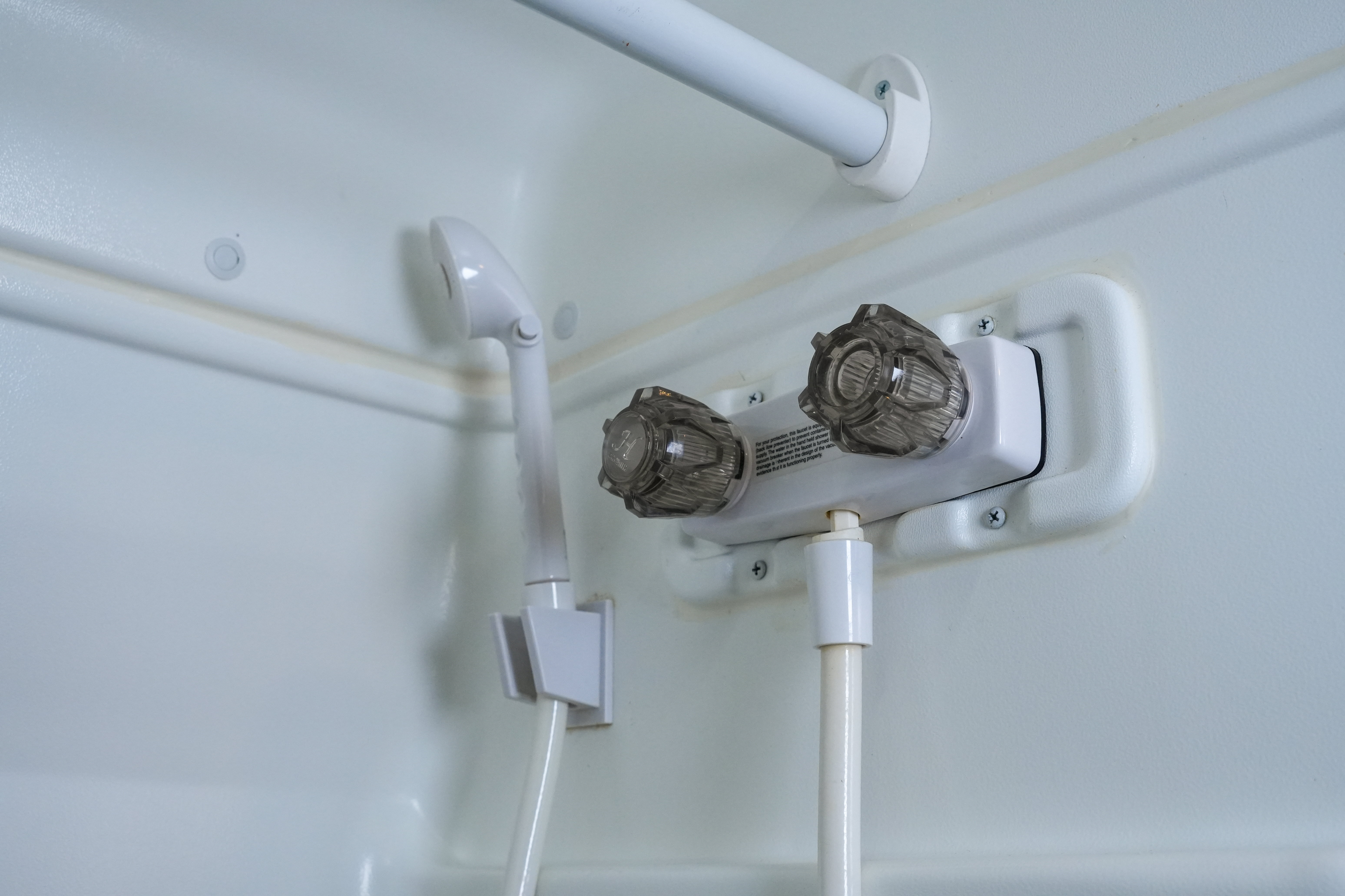 Close-up of a campervan shower with handheld showerhead, two control knobs, and white interior walls.