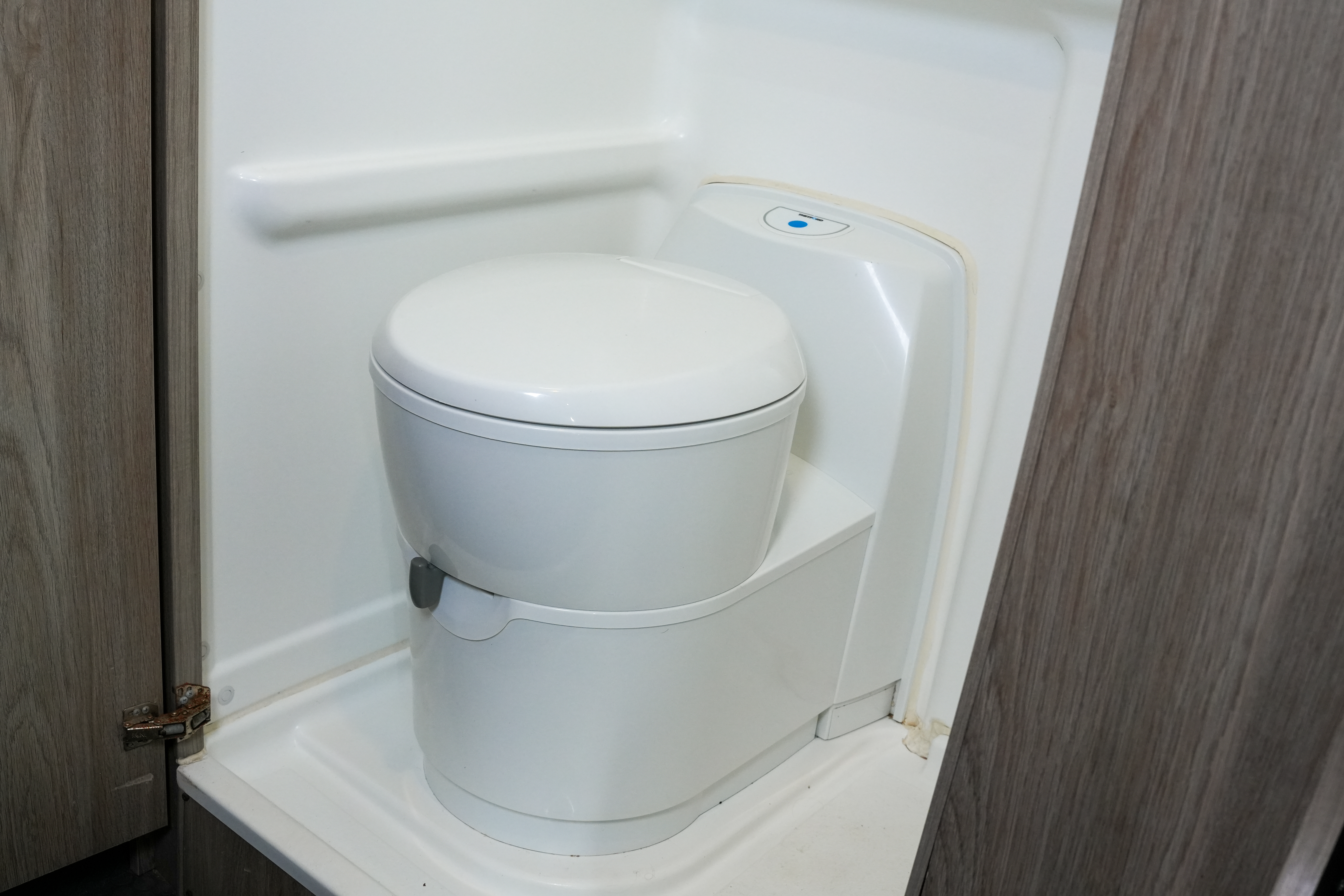 Compact white campervan toilet in a small private bathroom with light wood and white paneling.