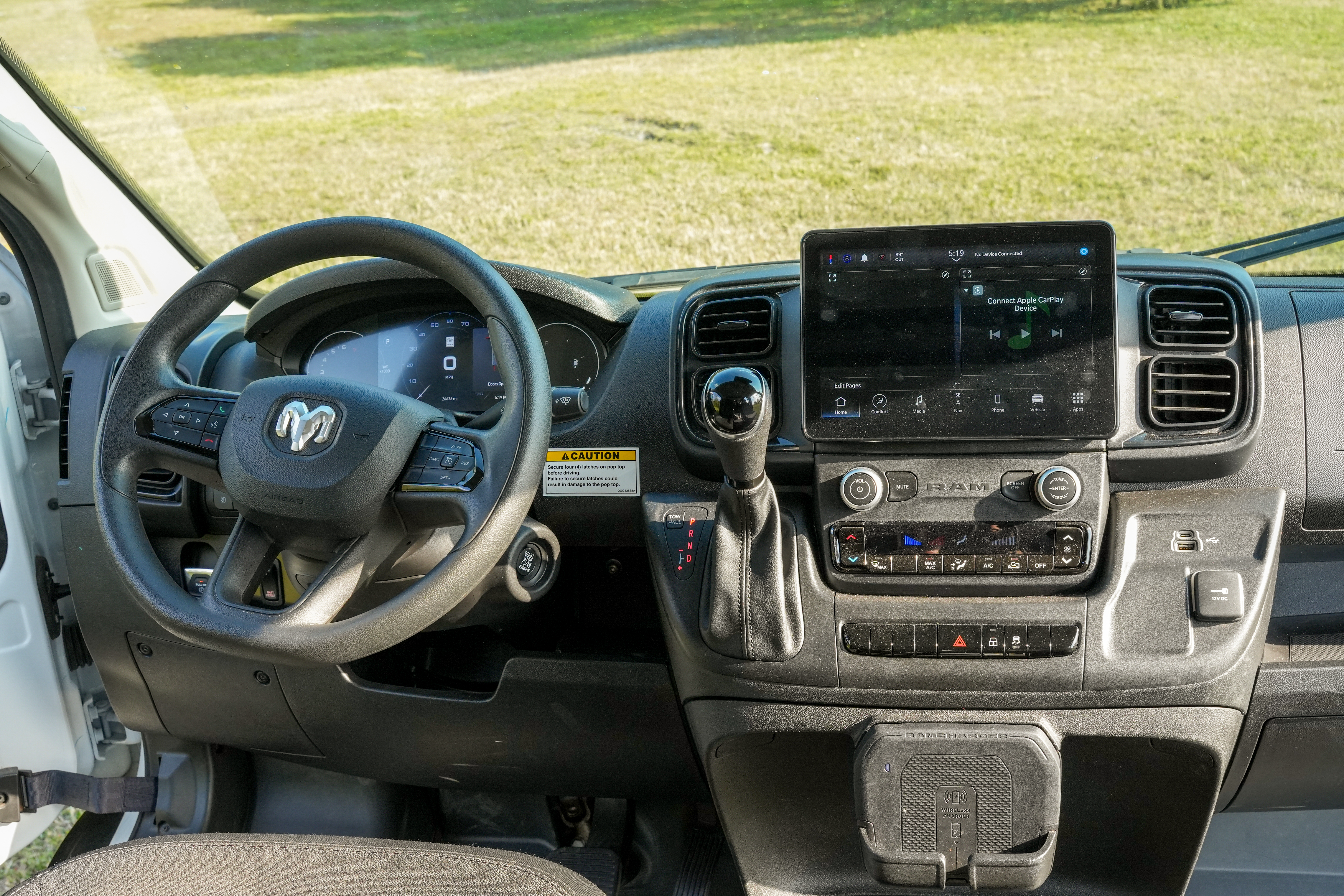 Modern camper van dashboard with steering wheel, touchscreen display, gear lever, and control panel, parked on grassy area.