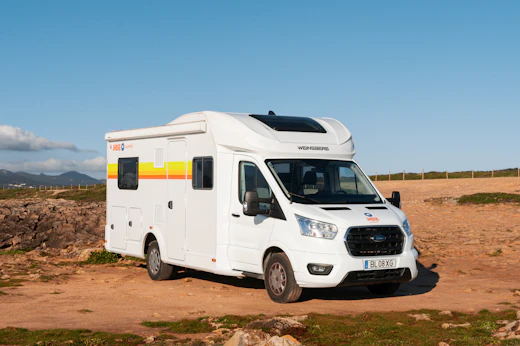 White campervan parked on a dirt road with clear blue sky and distant mountains in the background.