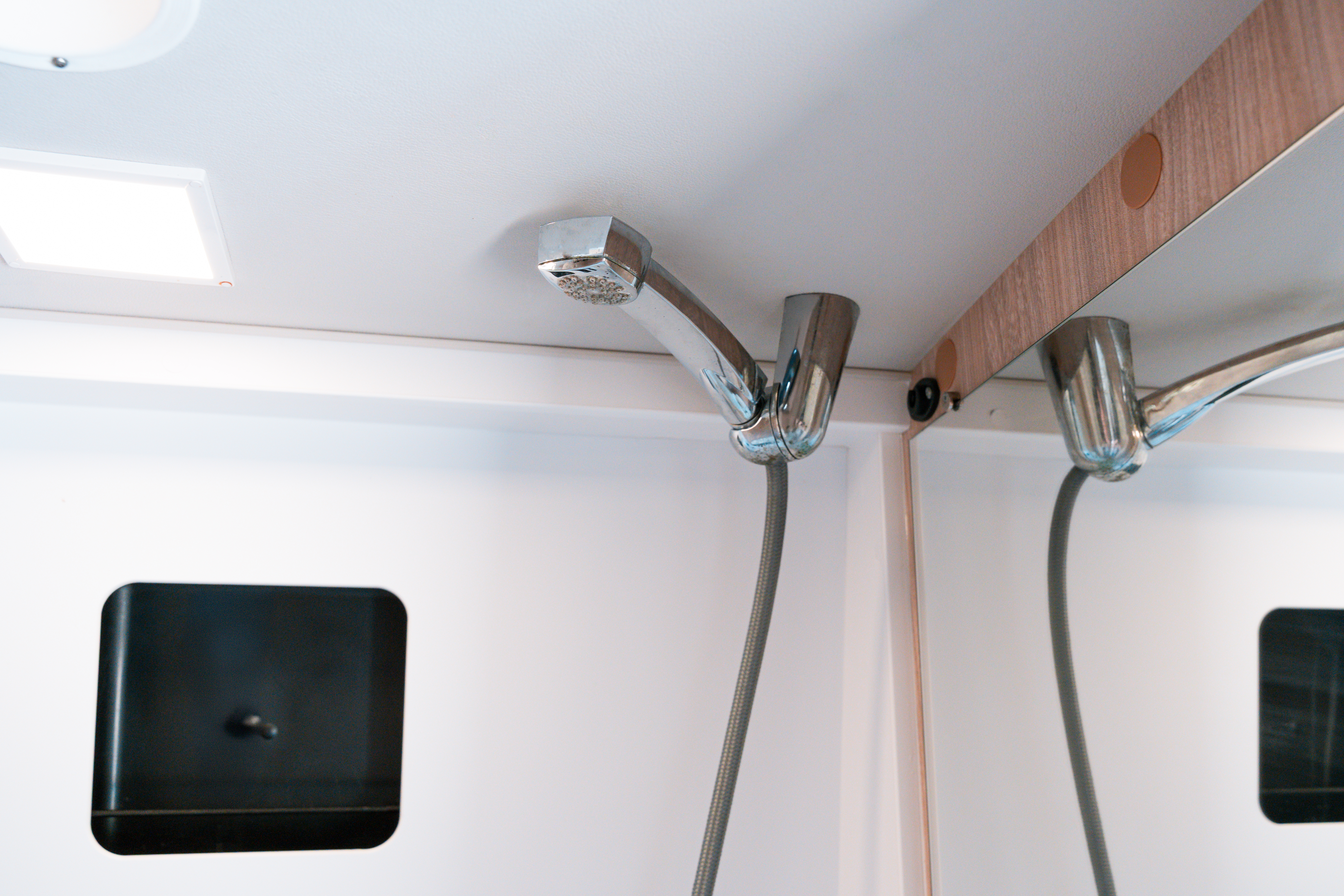 Close-up of a modern camper van showerhead and mirror inside a compact, clean bathroom space.