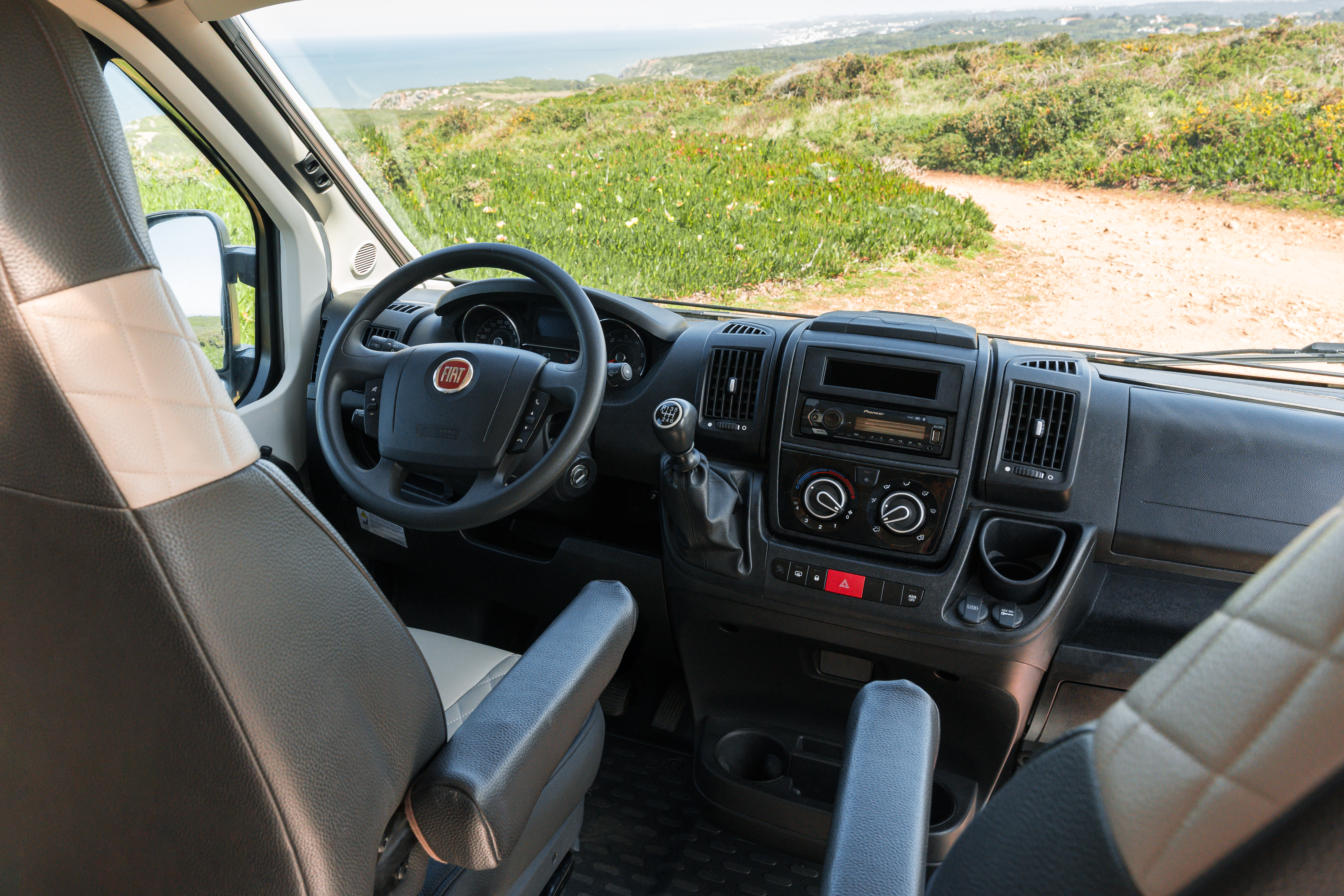 Campervan interior showing driver’s seat and dashboard, with scenic countryside visible through the windshield.