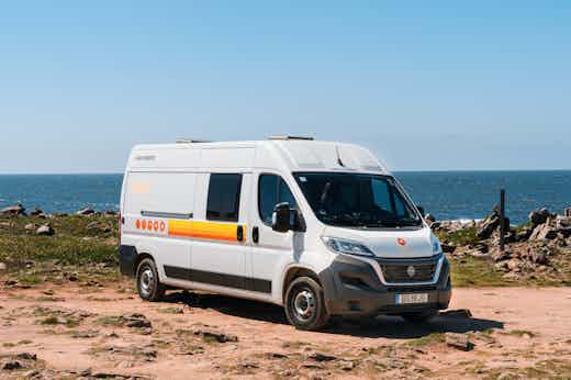 Active Bunk EU Hero White camper van parked on a rocky coastal landscape with ocean and clear blue sky in the background.